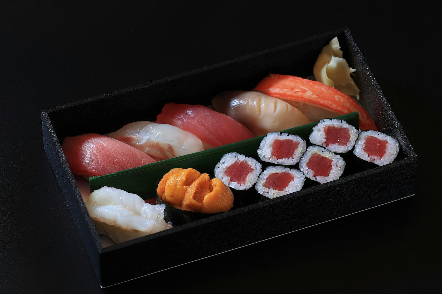 Piring sushi yang indah dengan berbagai jenis sushi dan gulungan di latar belakang hitam