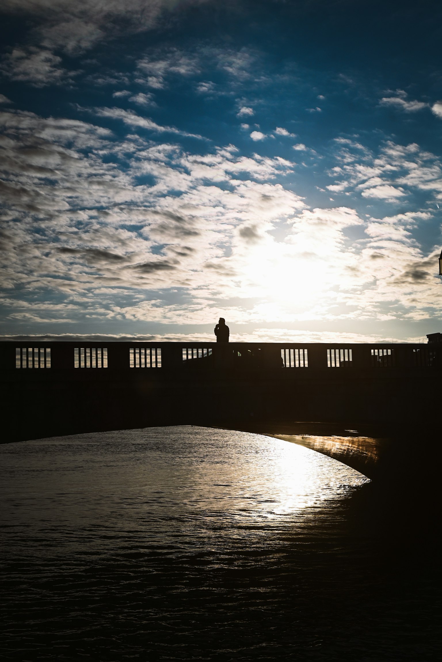 Silhouette di un ponte contro il tramonto con riflessi sull'acqua