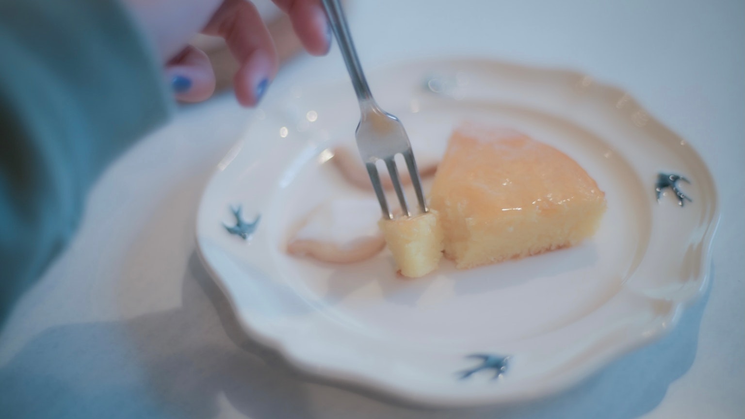 A hand holding a fork cutting a piece of cake from a decorative plate
