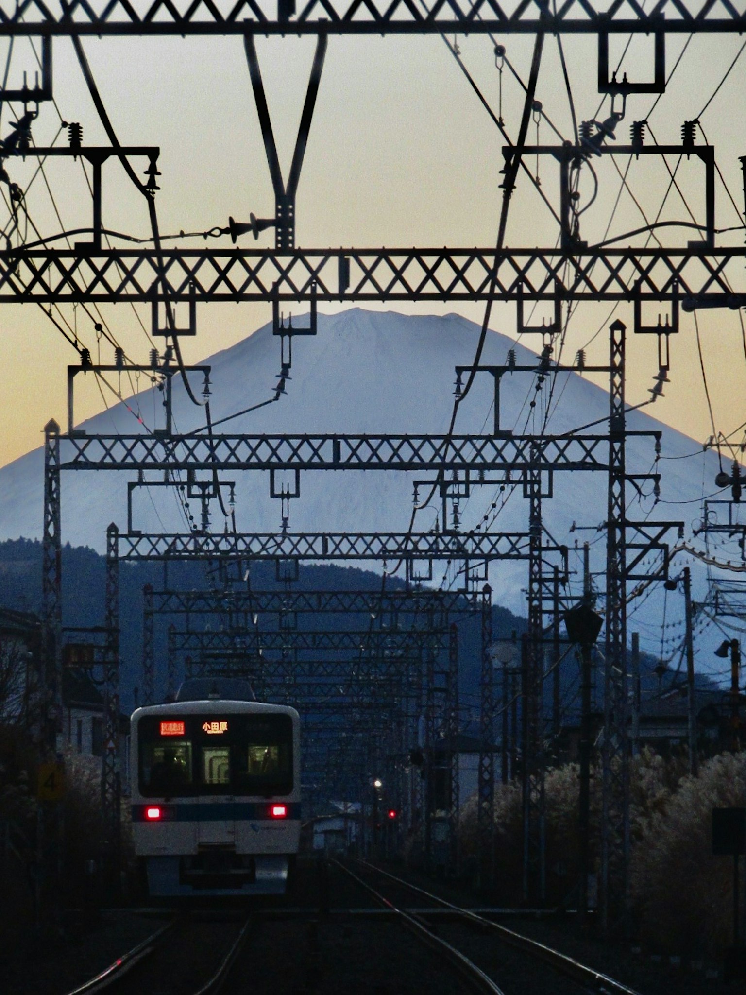 รถไฟกำลังเข้าใกล้ภูเขาฟูจิที่อยู่เบื้องหลังมีสายไฟฟ้าล้อมรอบ