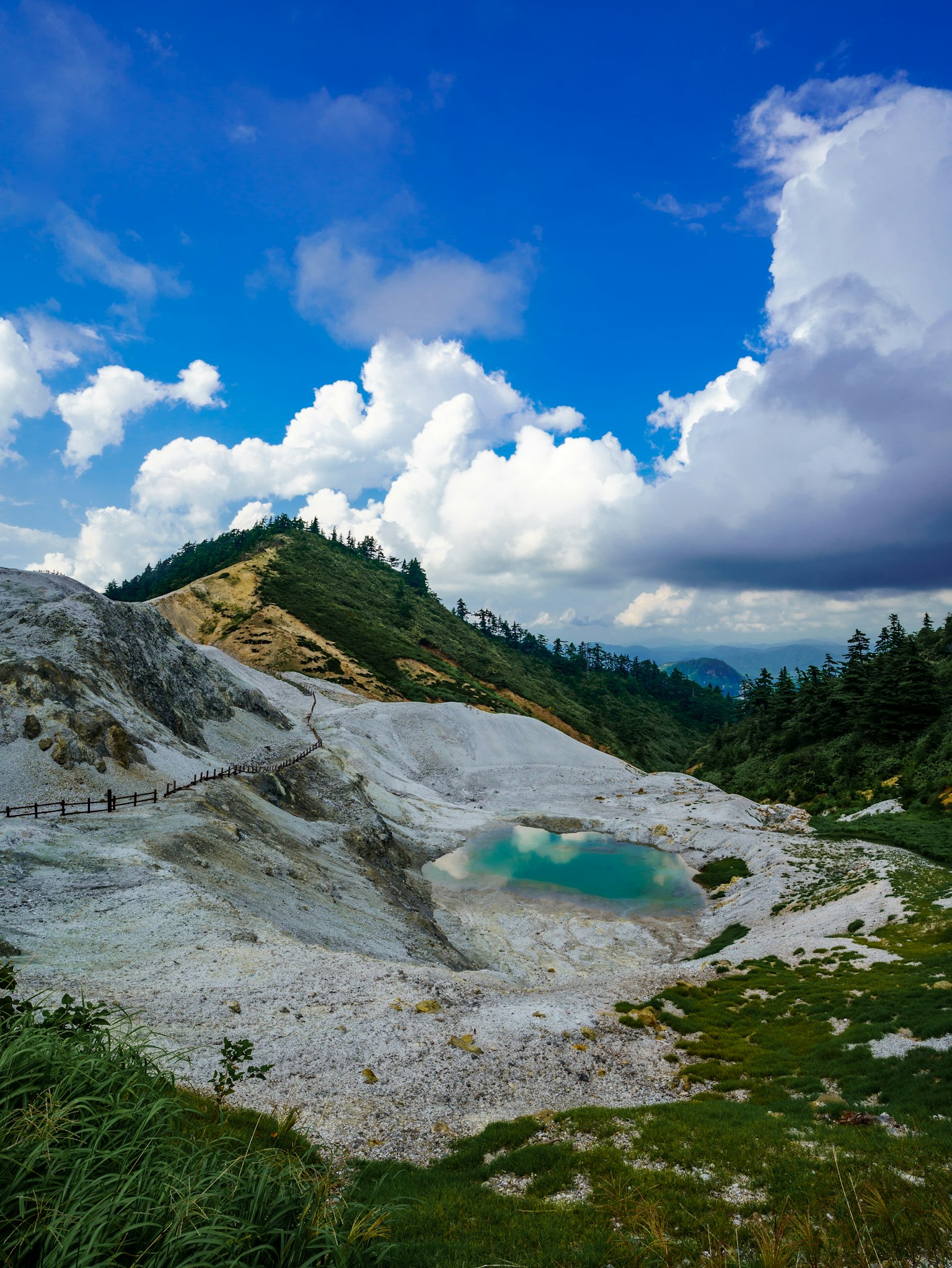 ทิวทัศน์ที่สวยงามใต้ท้องฟ้าสีฟ้าพร้อมเมฆสีขาวมีหญ้าสีเขียวและบ่อสีน้ำเงินบนเนินเขา
