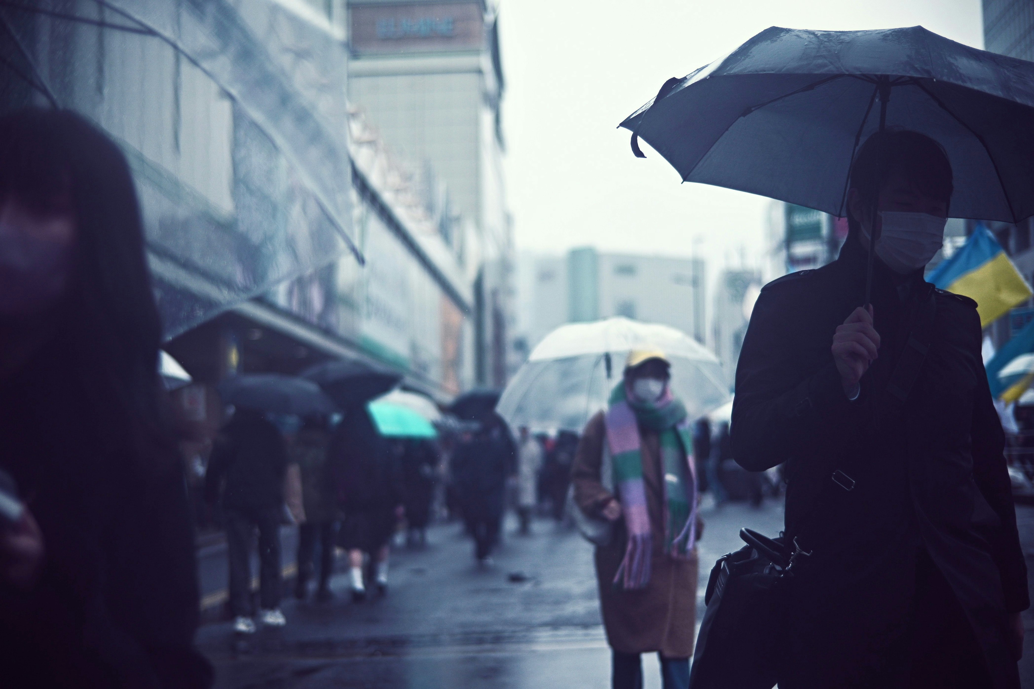 雨の路地を傘をさして歩く人々のスナップ