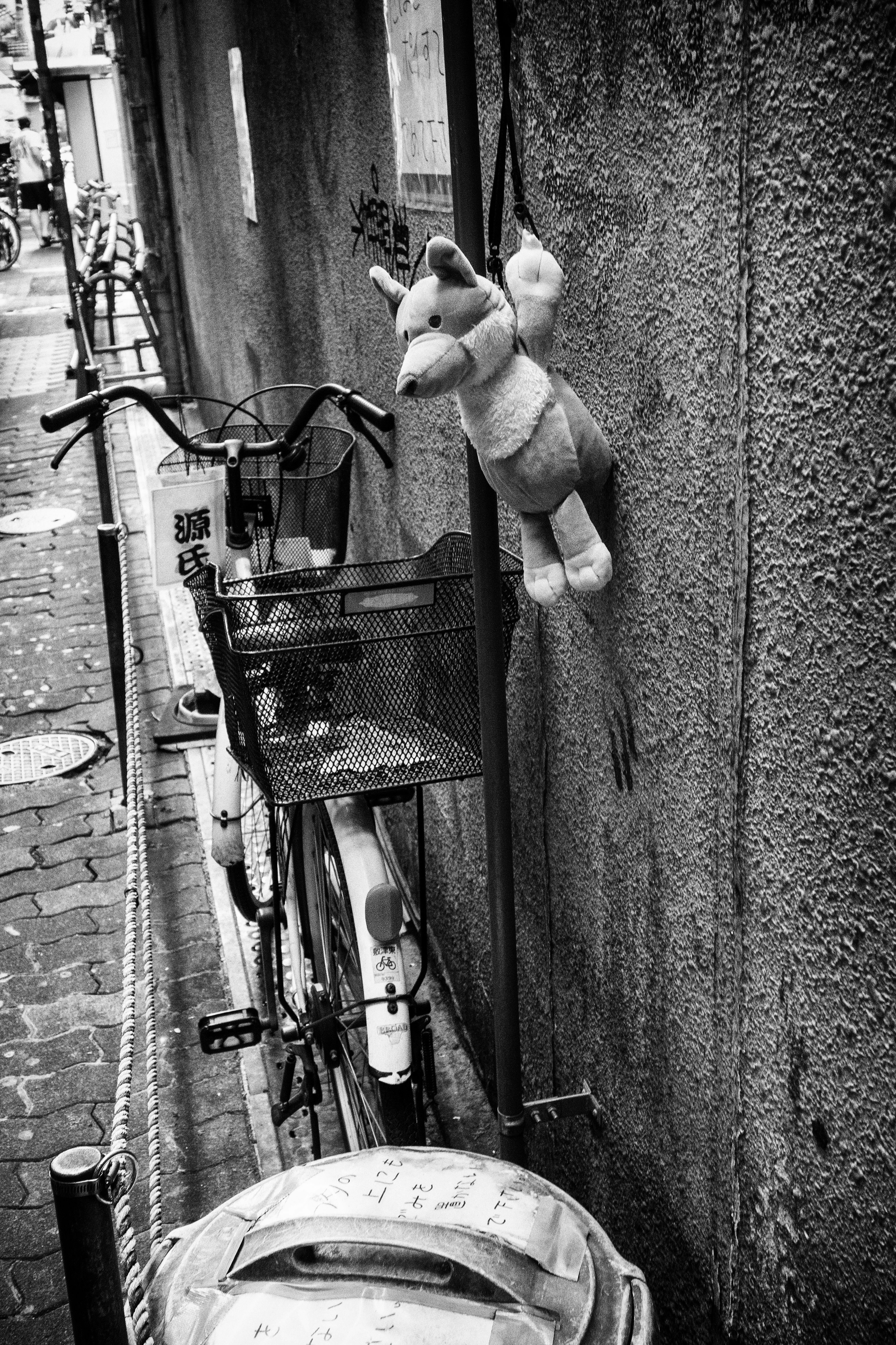 路地の壁際に並ぶ自転車とぬいぐるみ
