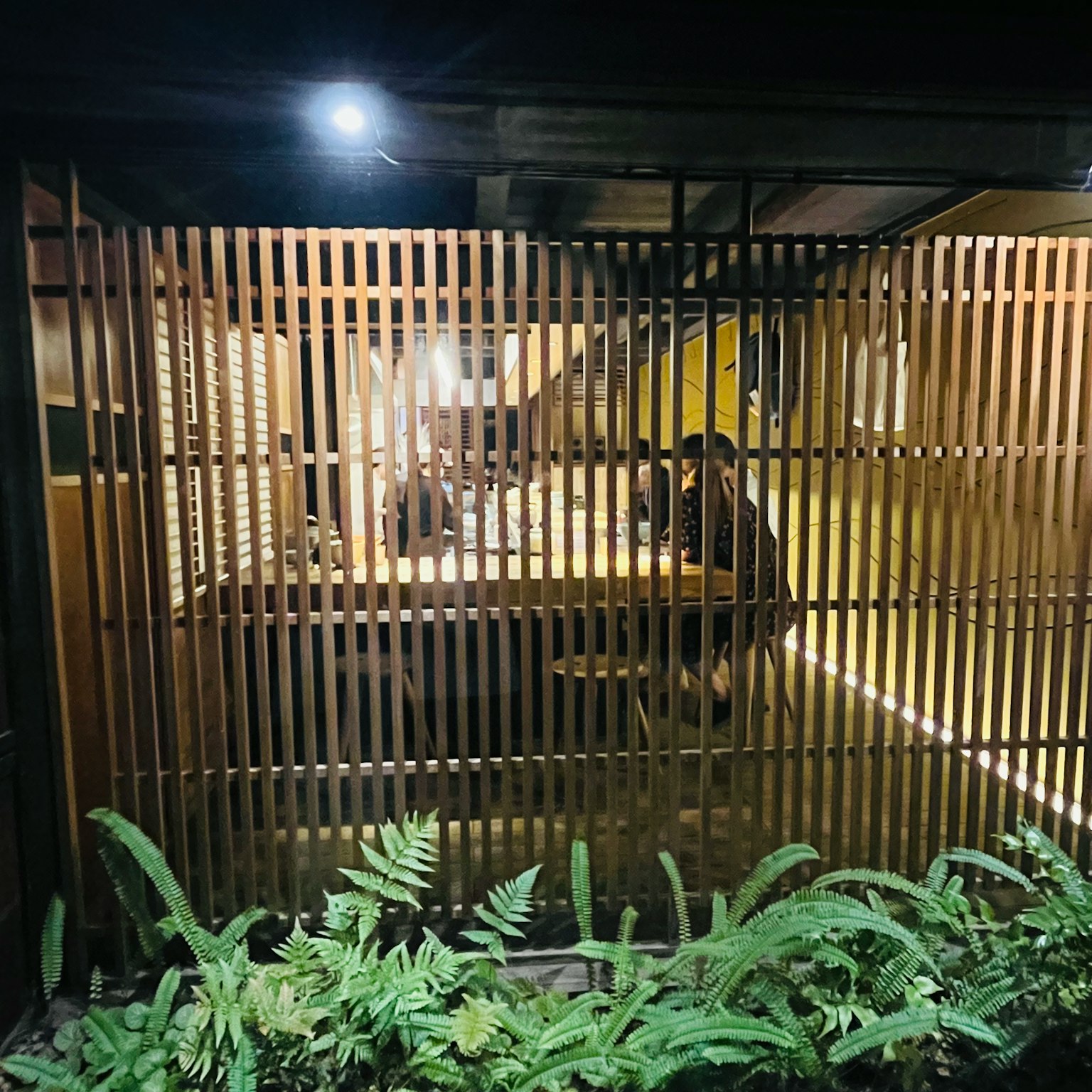Cozy room enclosed by wooden slats with a person sitting inside surrounded by greenery