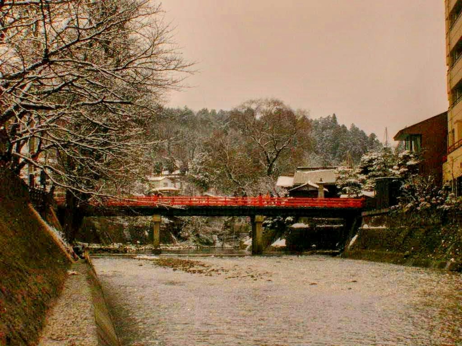 Scena di fiume innevato con un ponte rosso