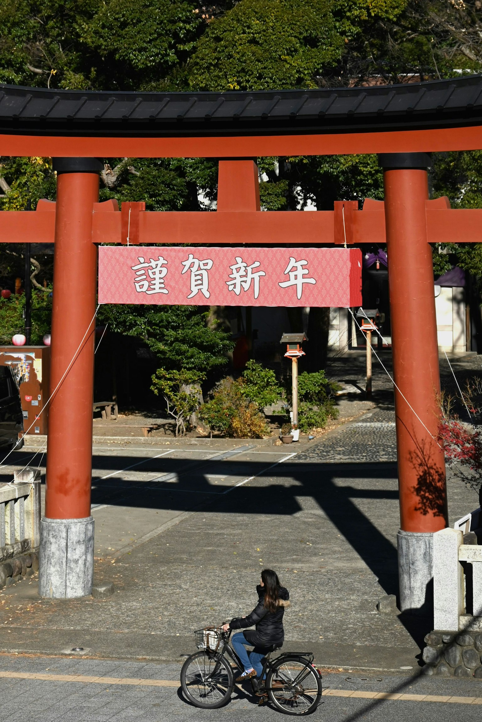 Woman riding a bicycle under a red torii gate New Year's greeting sign in Japanese