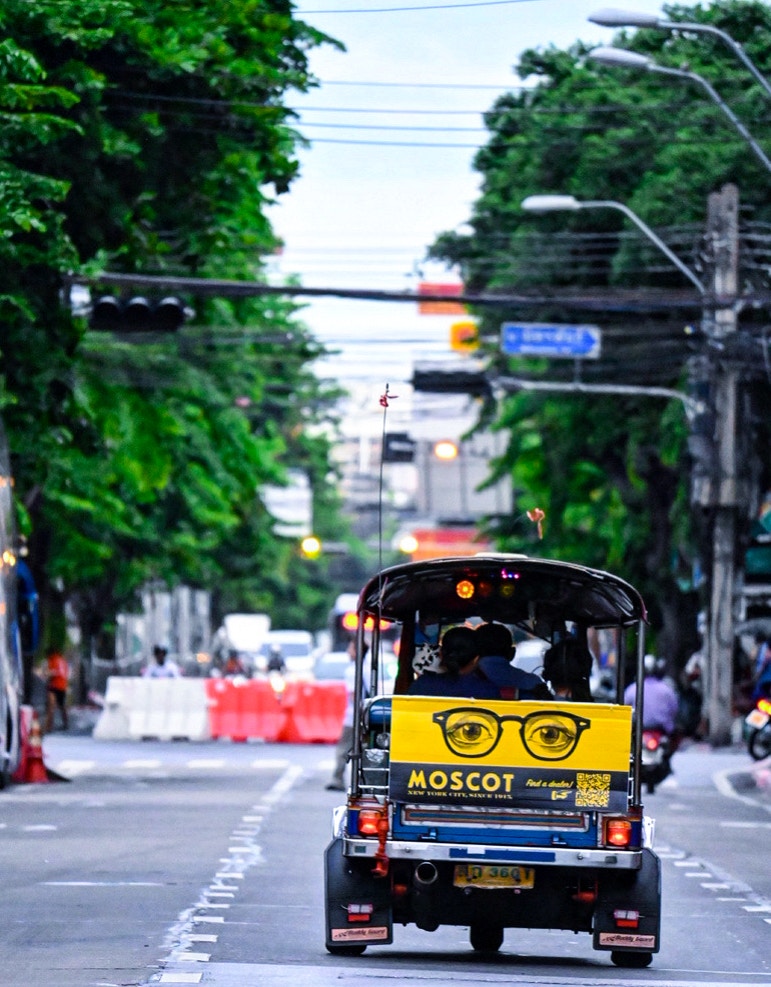Vista trasera de un tuk-tuk en una calle arbolada cartel amarillo con ilustración de gafas
