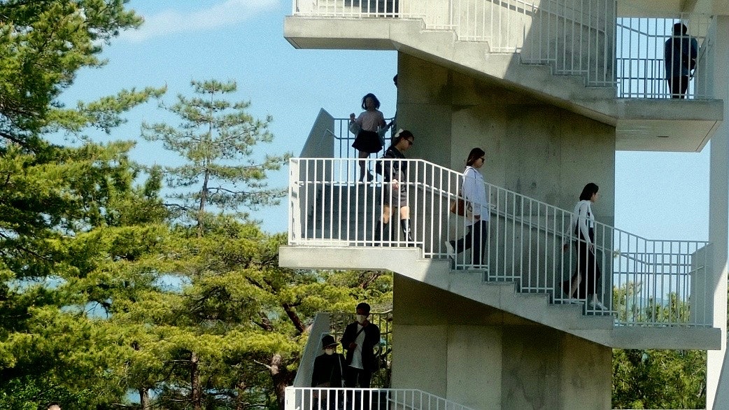 緑の木々の中にある階段状の建物で人が見学する風景