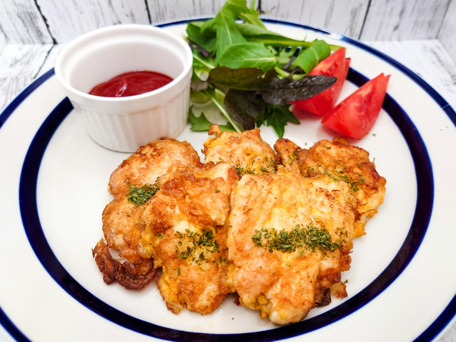 Pollo fritto croccante su un piatto con insalata pomodori e un contorno di ketchup