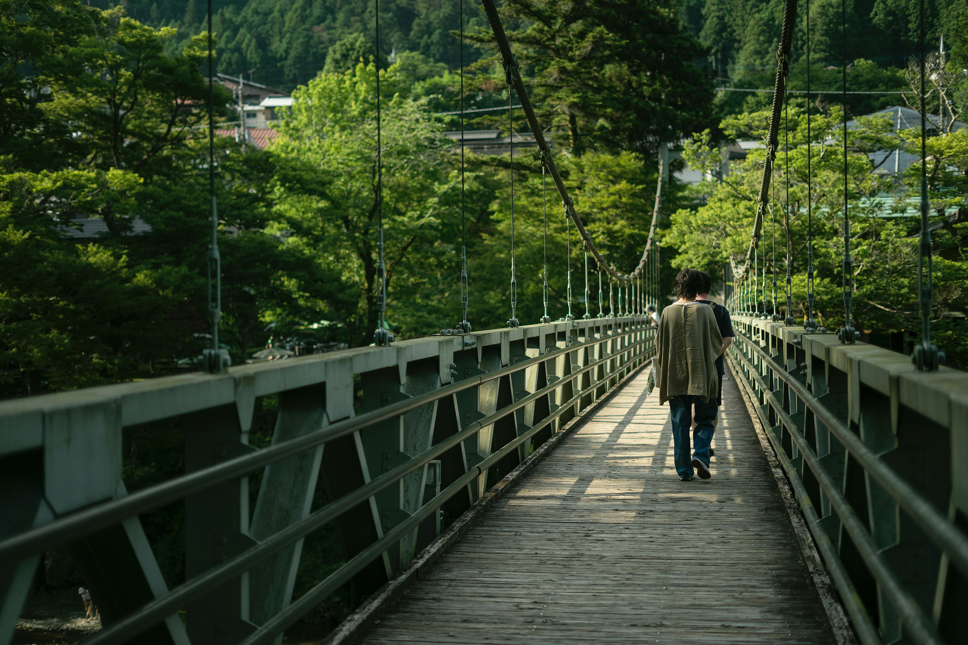 a person walking on a suspension bridge surrounded by greenery of Mt. Ontake