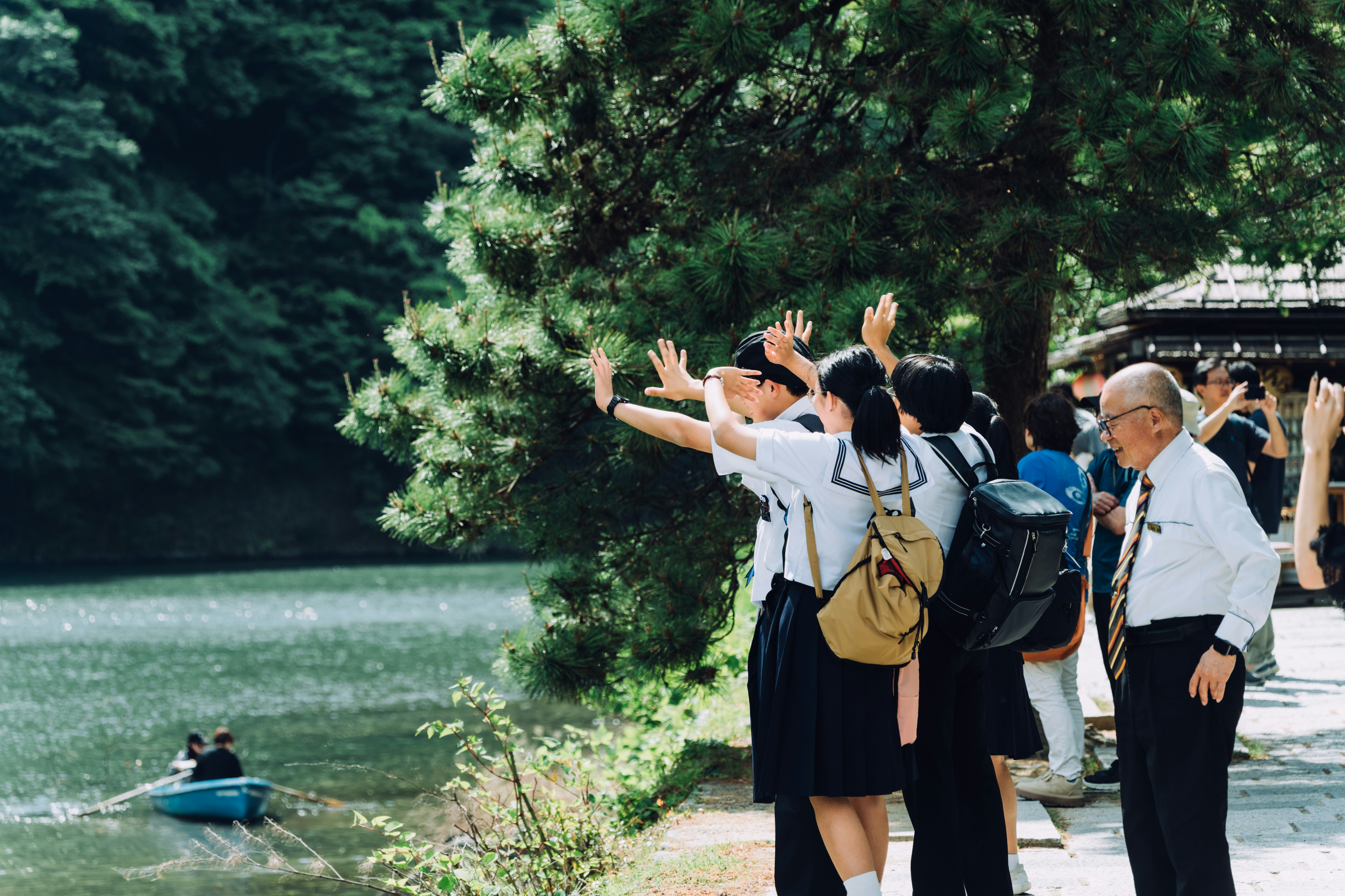 木々の並ぶ道で手を上げる人々と遠ざかるボート