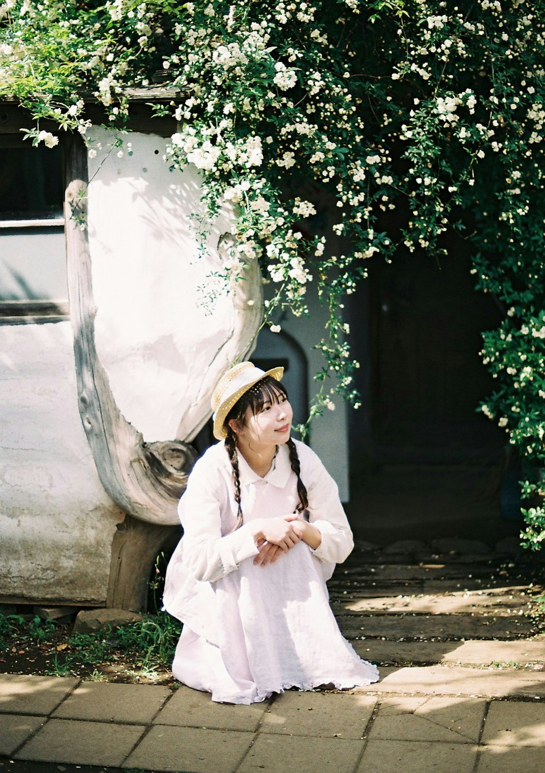 白い花に囲まれた石壁の前で微笑む少女