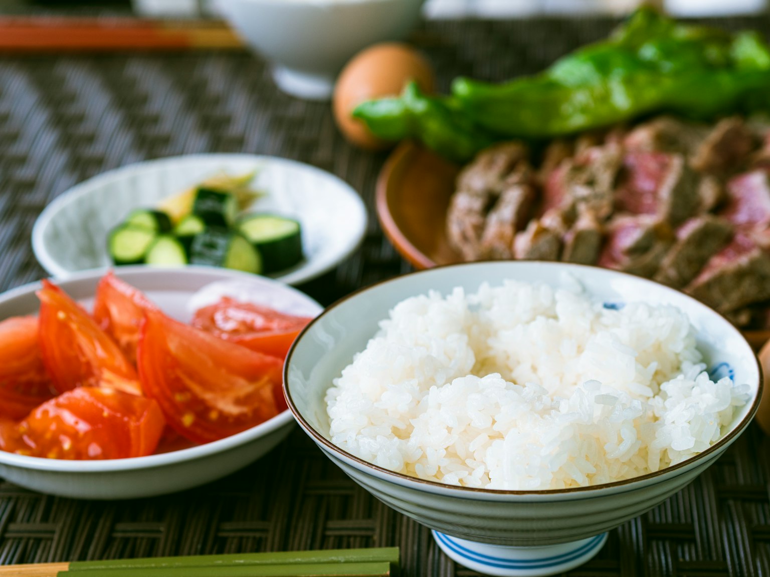 Bàn ăn với cơm trắng, cà chua cắt lát, dưa chuột và thịt nướng