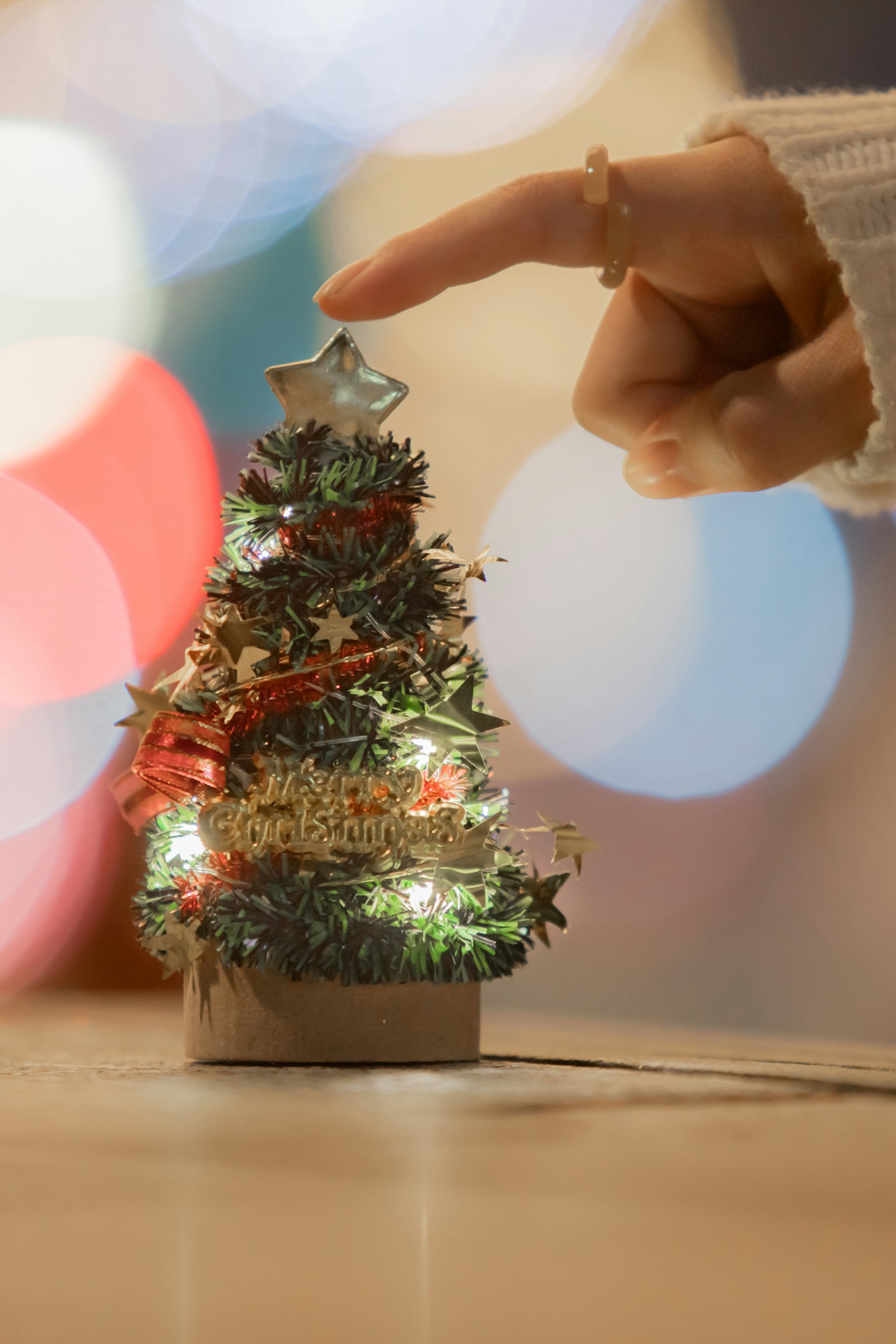 Una mano che tocca un piccolo albero di Natale con luci sfocate sullo sfondo