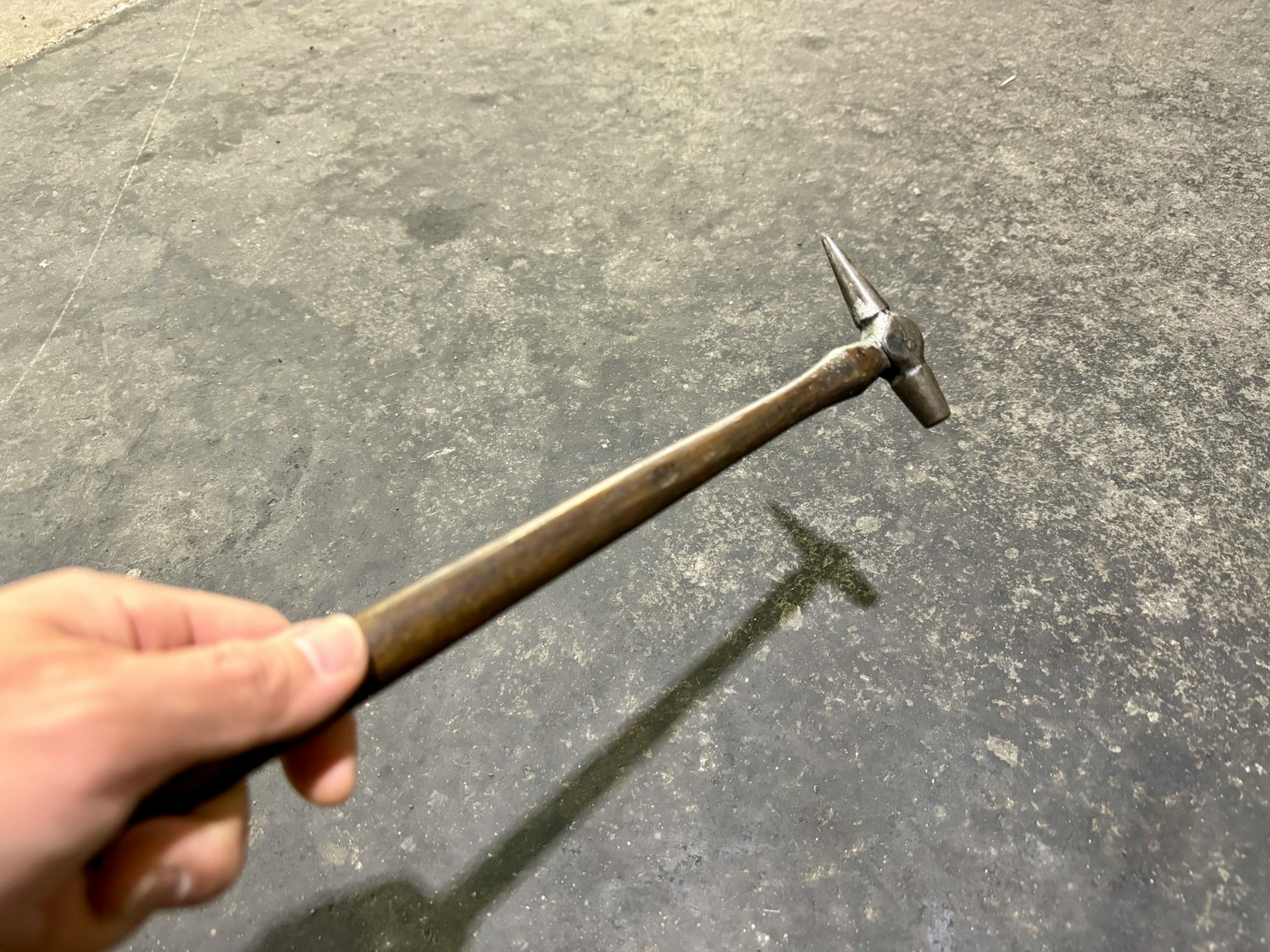 Un martello di metallo tenuto in mano che proietta un'ombra su un pavimento in cemento