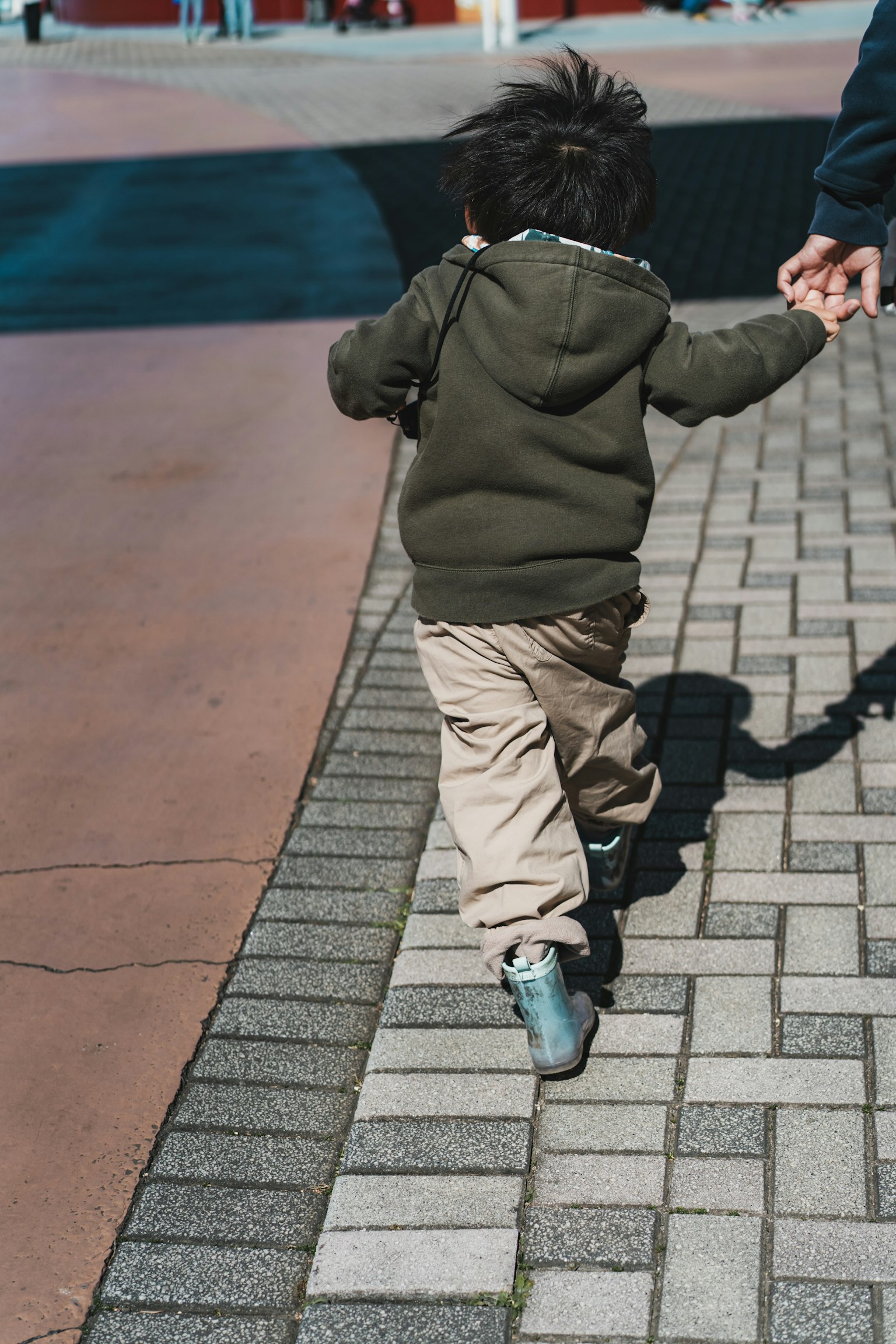 Ein kleines Kind, das Hand in Hand mit einem Erwachsenen auf einem gepflasterten Weg geht