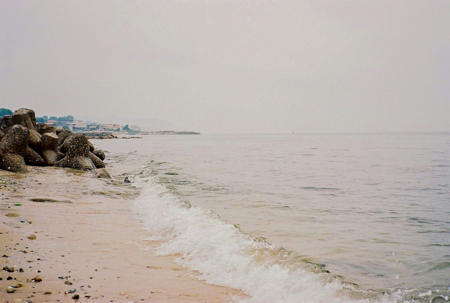 Calm waves lapping at a sandy beach under a gray sky
