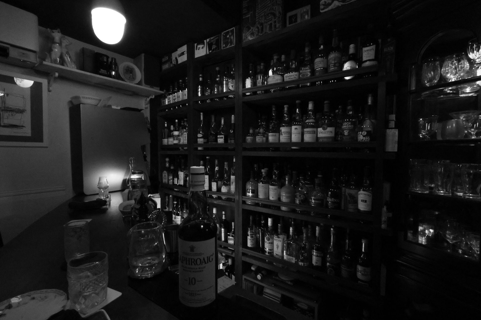 Interior de un bar con poca luz lleno de varias botellas y copas
