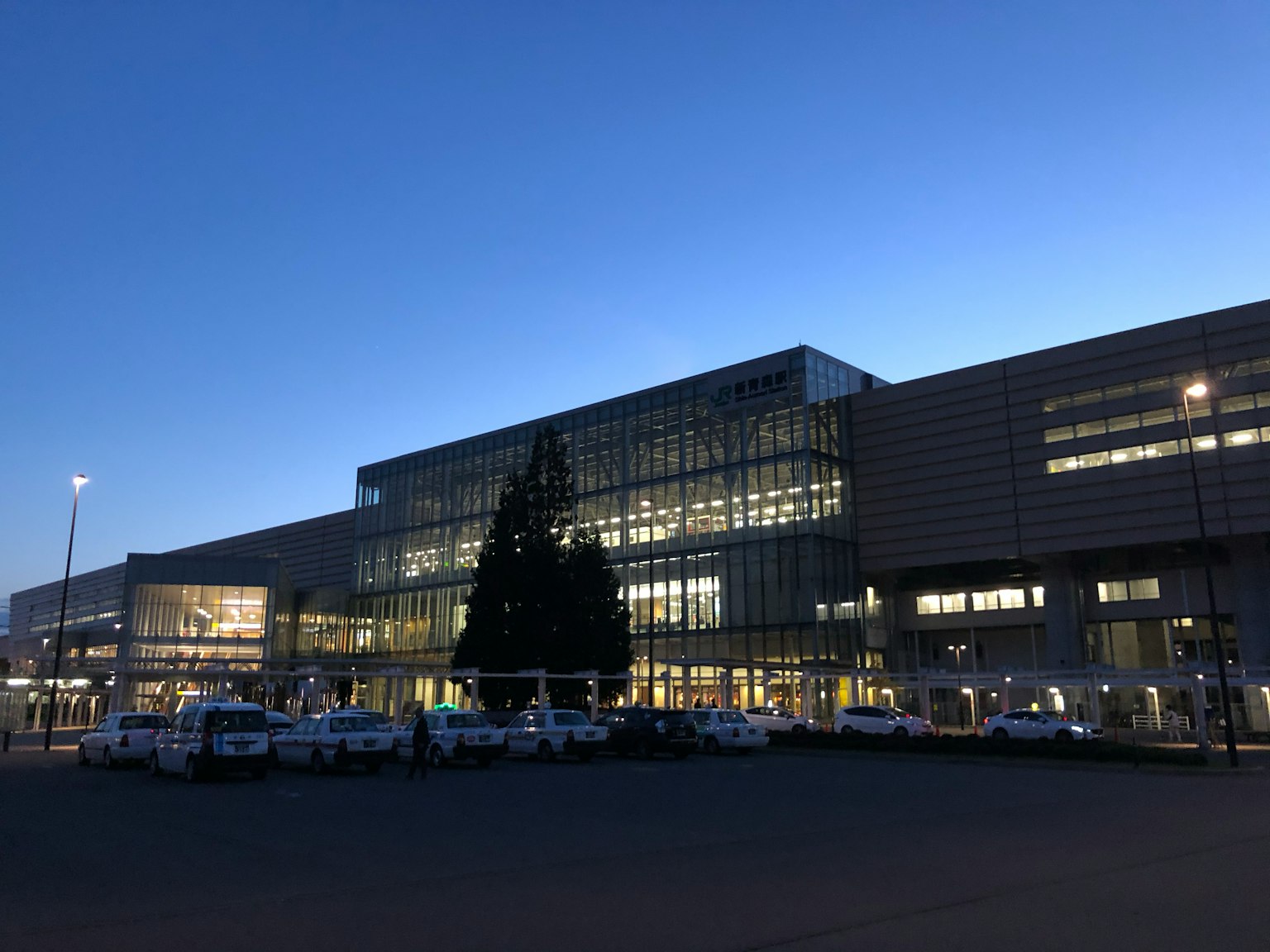 Modern airport building at dusk with illuminated facade and parked vehicles