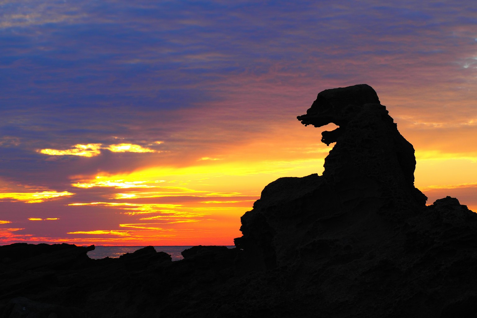 Silhouette einer hundeähnlichen Felsformation vor einem bunten Sonnenuntergang