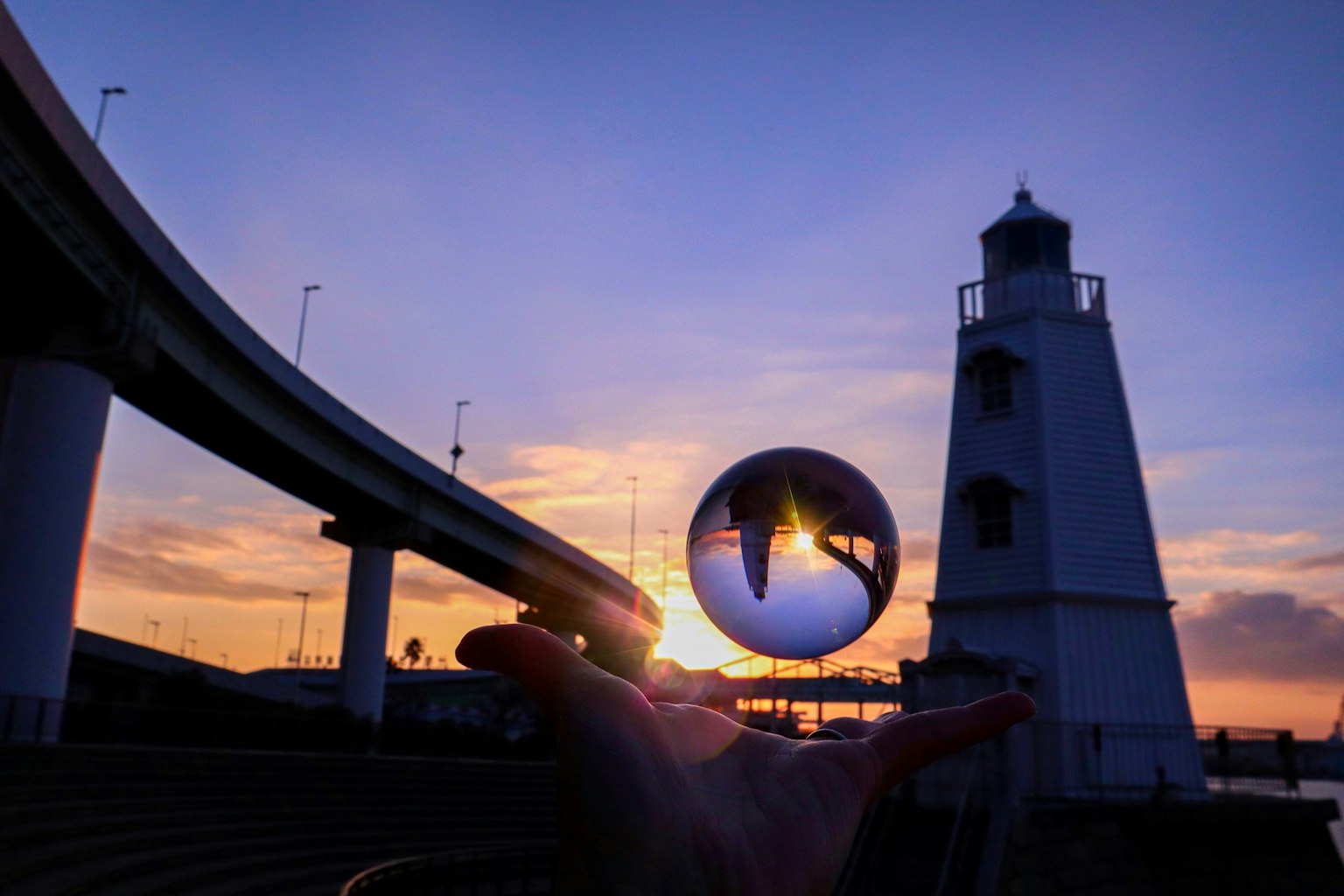 Une boule en cristal tenue dans une main reflétant un phare au coucher du soleil