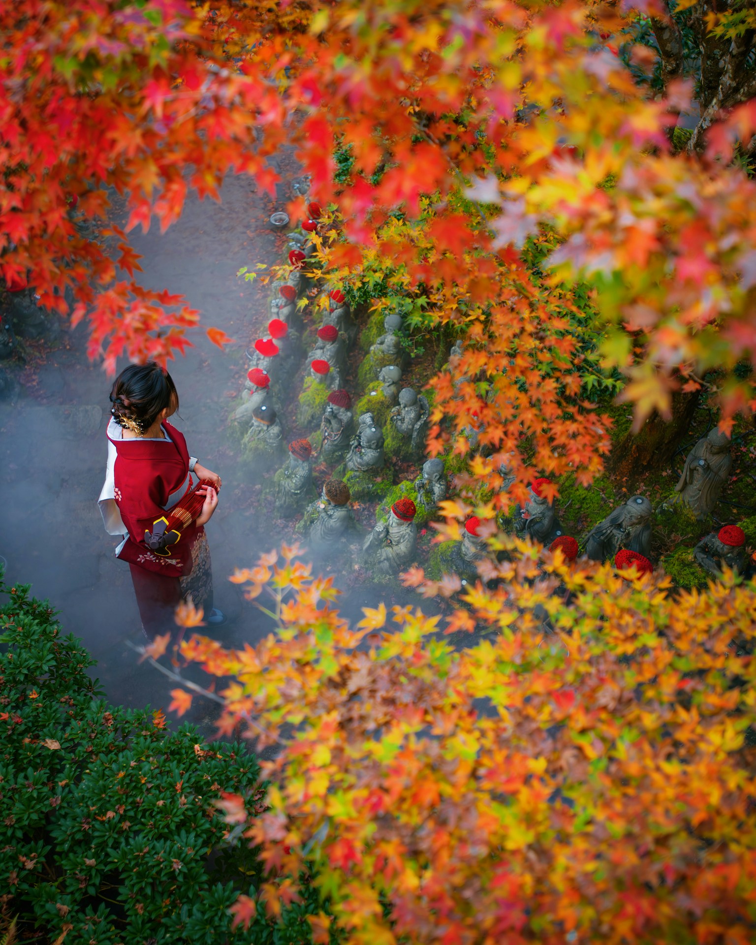 A girl in a red kimono walking through mist surrounded by autumn leaves