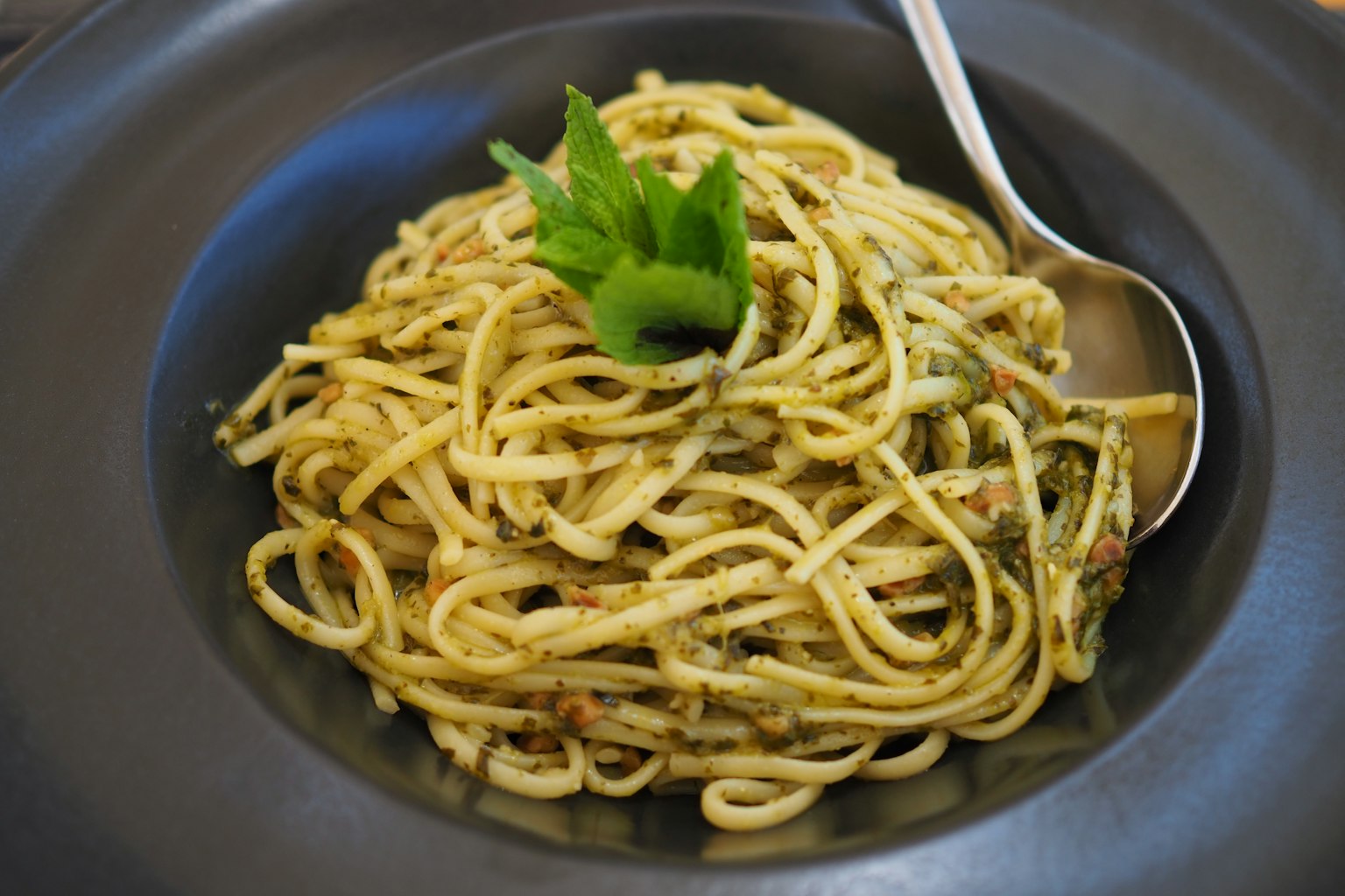 Spaghetti dihias dengan herbal hijau disajikan di atas piring hitam