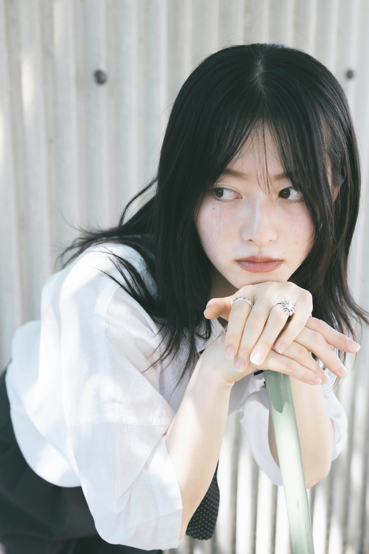 年轻女性长黑发，穿着白衬衫，双手托着下巴