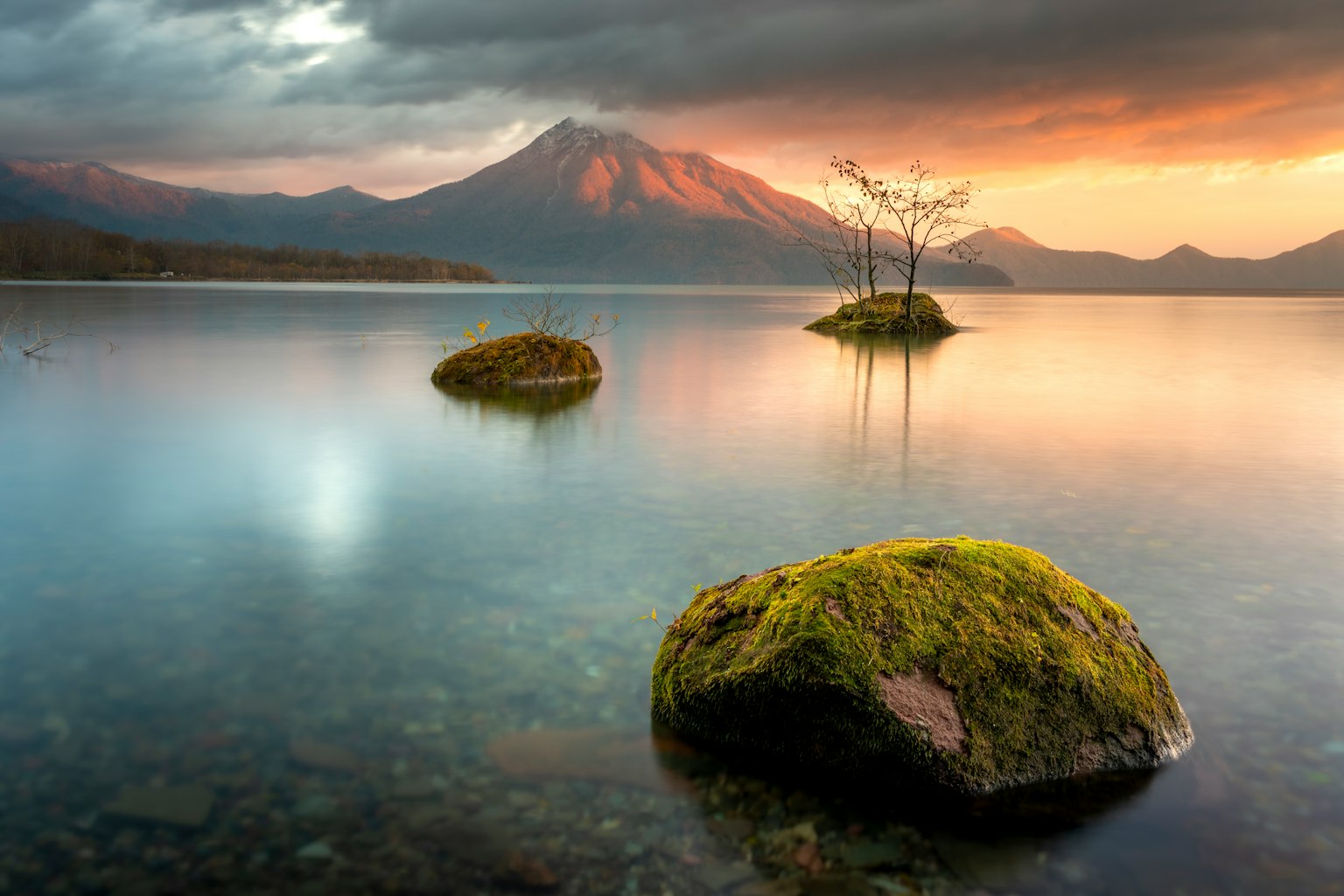 Vista escénica de un lago con rocas cubiertas de musgo y montañas distantes