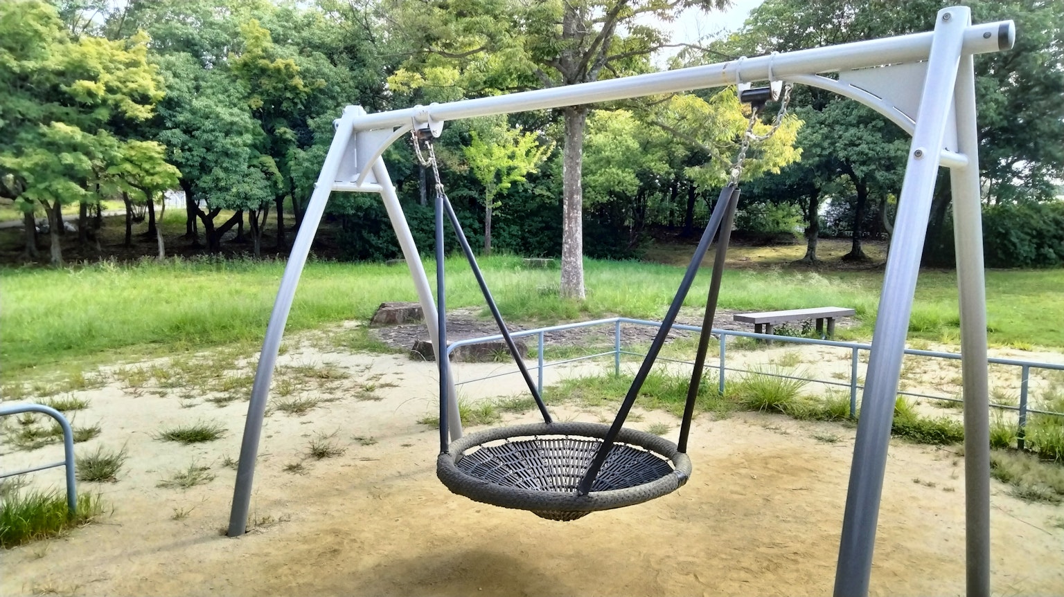 公園秋千的照片，金屬框架和黑色網座，周圍有綠色樹木