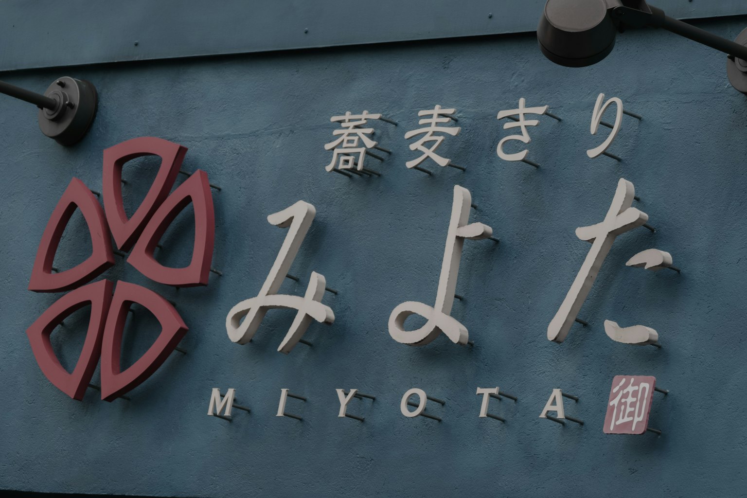 Schild für Miyota mit einem roten blumenähnlichen Design und weißen Buchstaben auf blauem Hintergrund