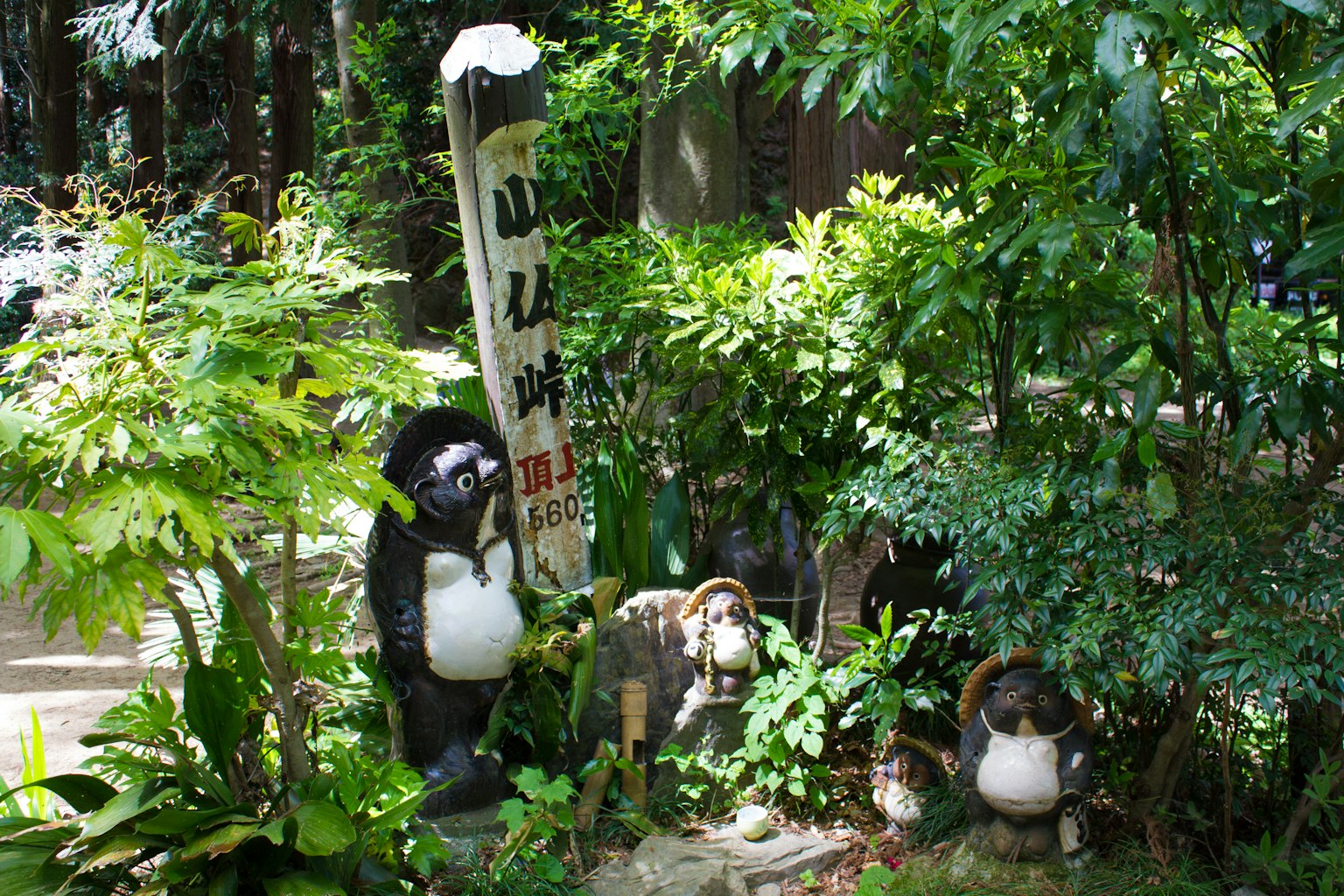 Sculptures de tanuki et un panneau dans un jardin verdoyant