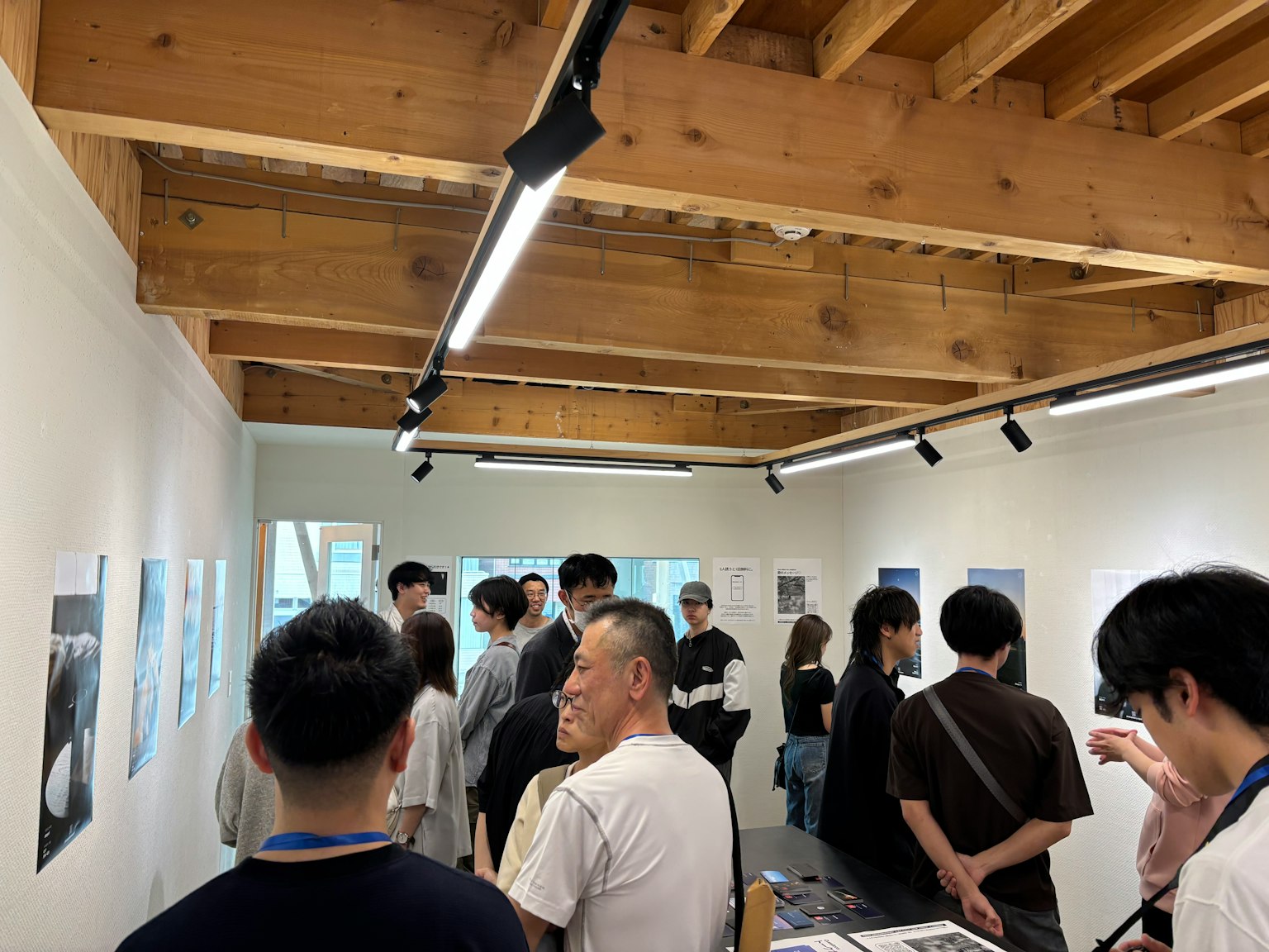 A gathering of people viewing photographs in a gallery with a wooden ceiling