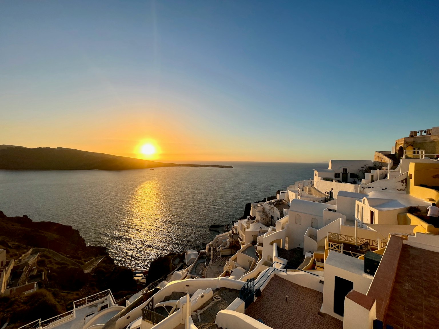 Weiße Gebäude entlang der Küste von Santorini mit einem Sonnenuntergang
