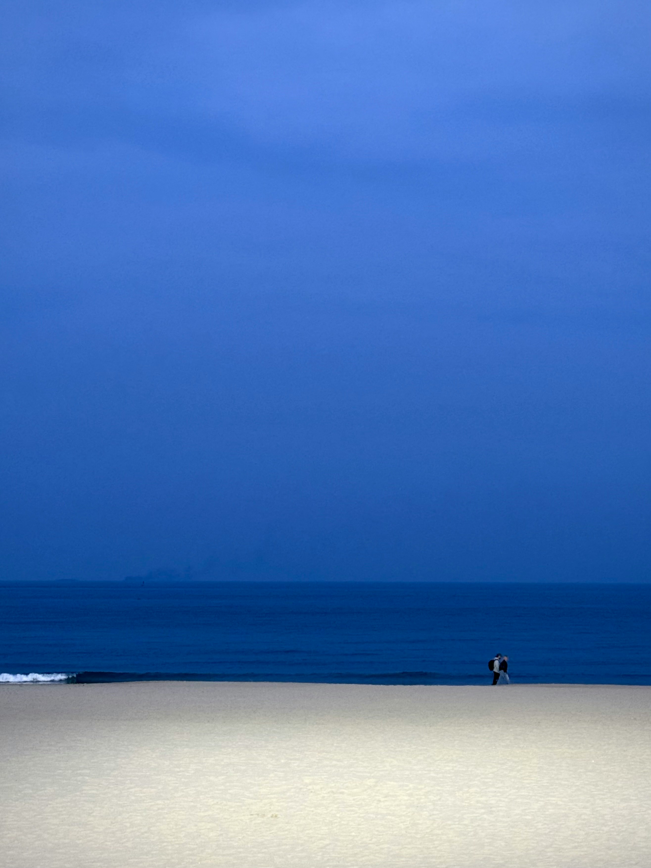 wide empty beach at blue hour with a small figure