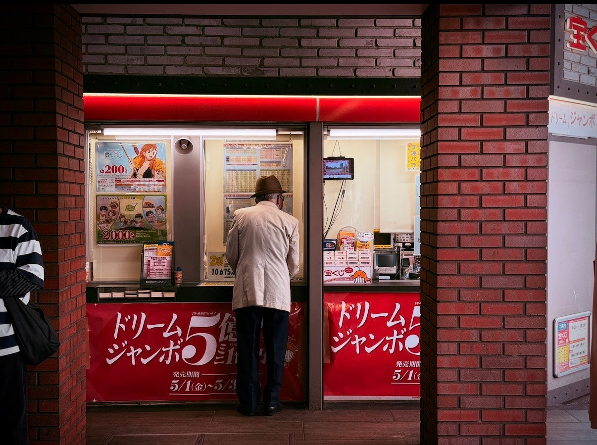 レンガ造りの建物の前で宝くじ売り場に立つ男性