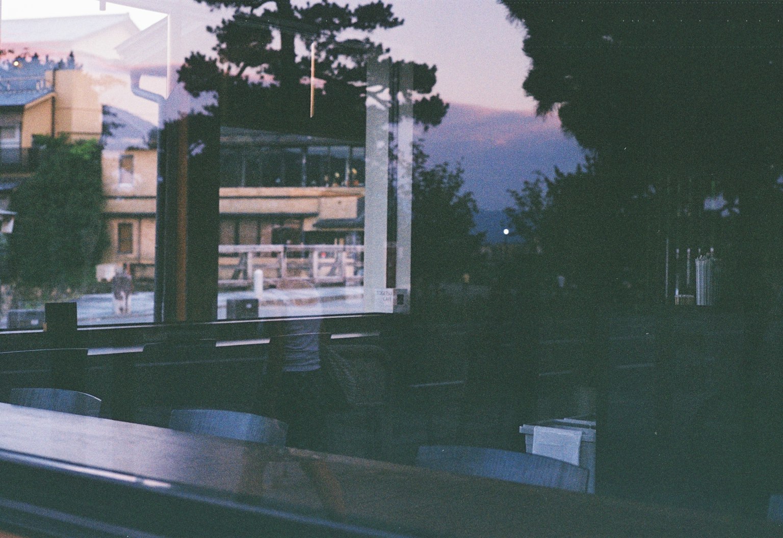 Blick auf eine Sonnenuntergangslandschaft und Gebäudespiegelungen durch ein Fenster