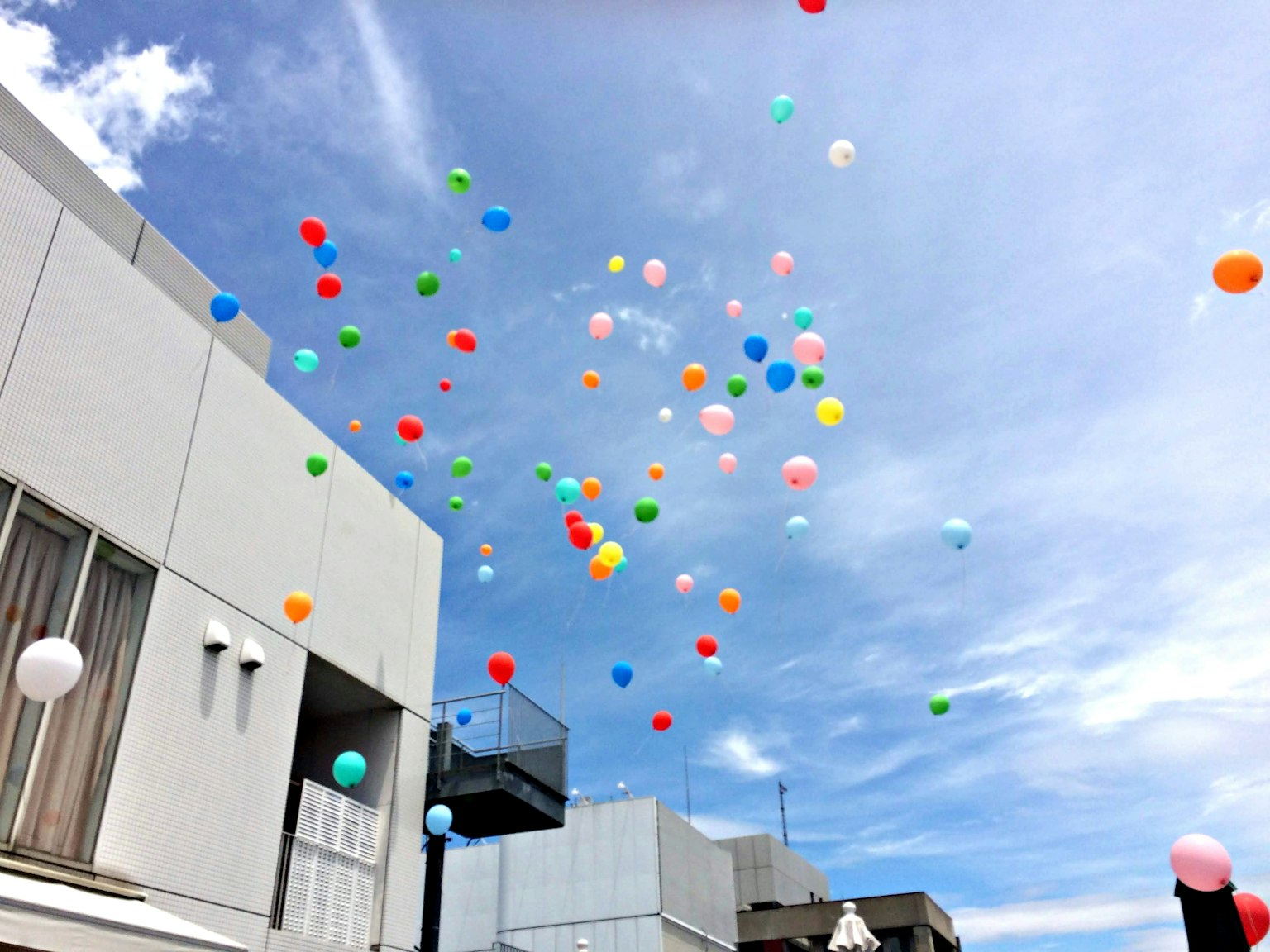 Balon berwarna-warni melayang di langit biru dengan bangunan putih