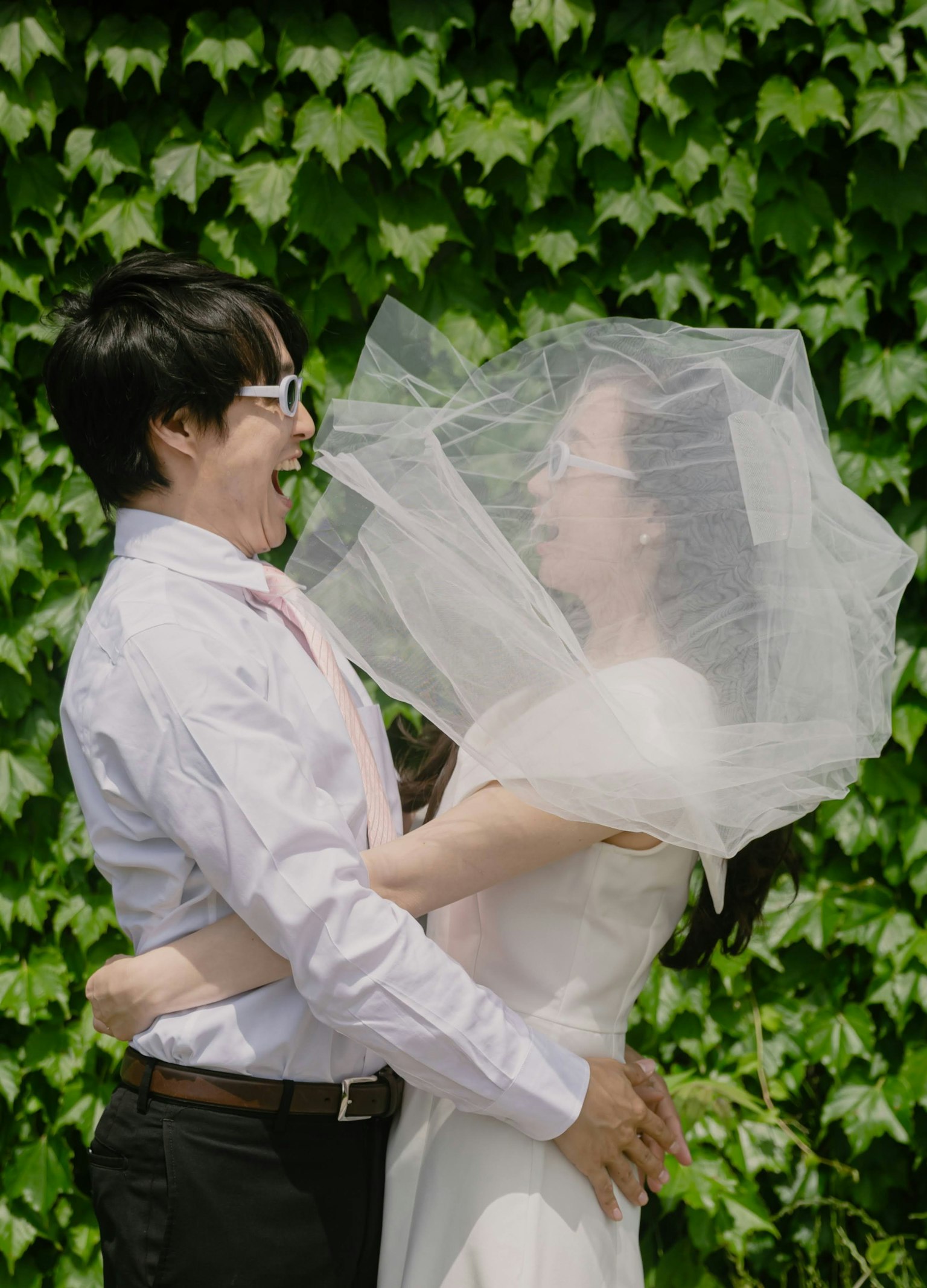 Một cặp đôi ôm nhau vui vẻ trước nền cây thường xuân xanh