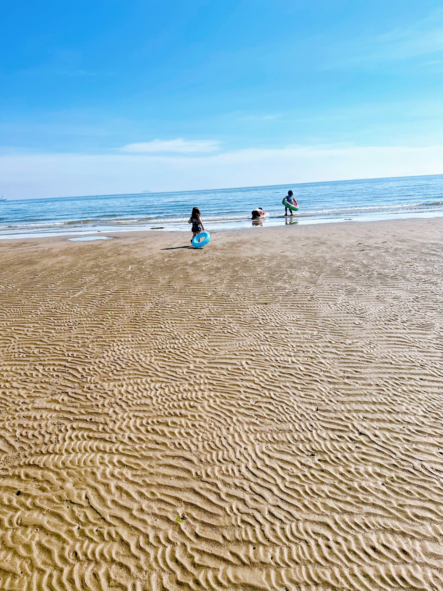 Anak-anak bermain di pantai dengan langit biru dan laut tenang