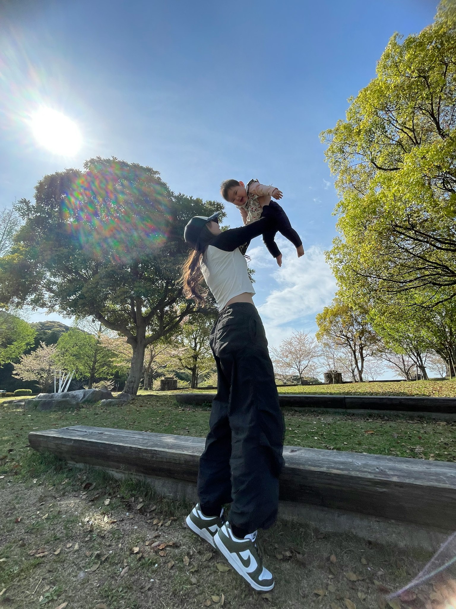 公園で赤ちゃんを抱き上げる女性の姿と青空