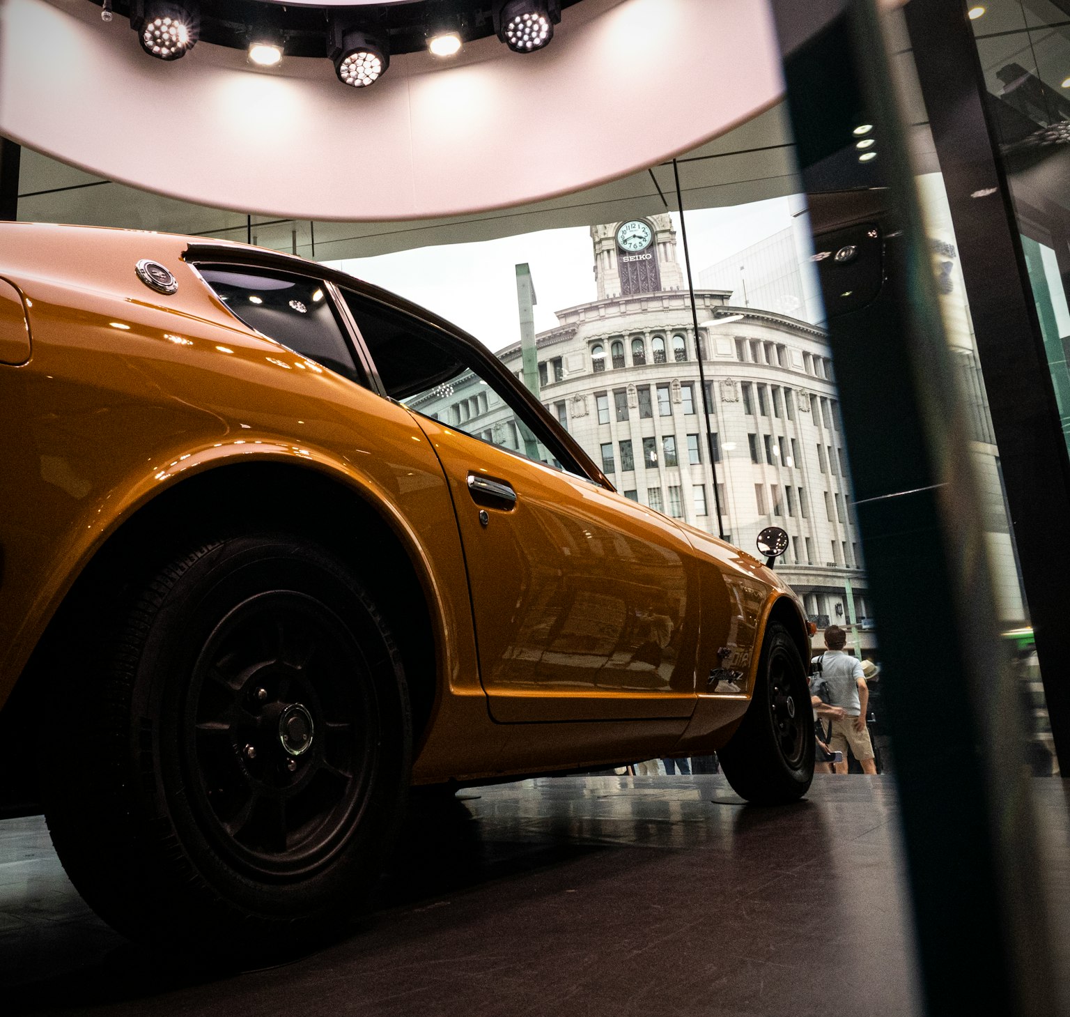 Orange Sportwagen durch ein Glasfenster mit einer Uhr im Hintergrund gesehen