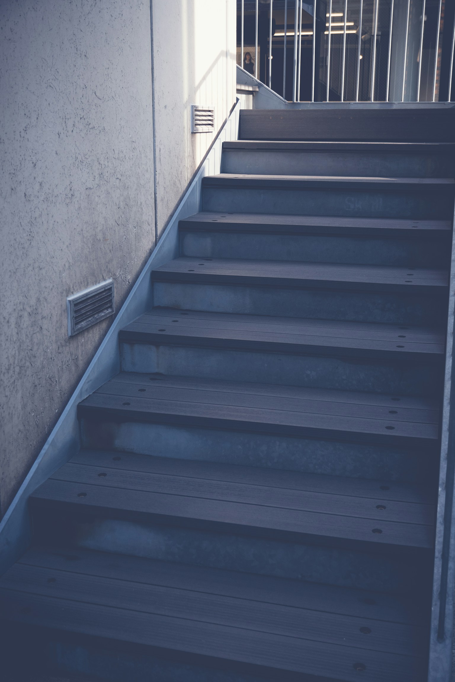 ภาพใกล้ของบันไดที่มีขั้นบันไดไม้และผนังคอนกรีตที่ถูกแสงสว่างส่องถึง