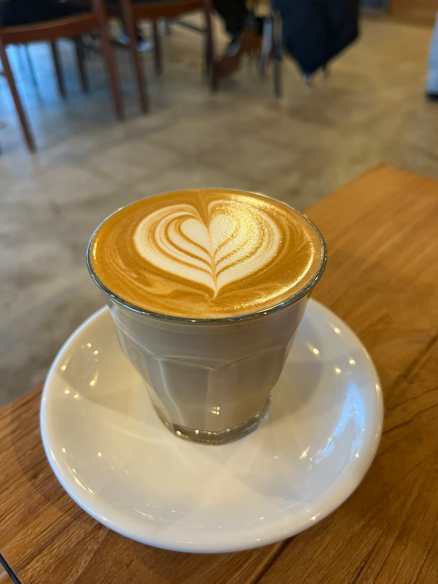 Eine Glastasse Latte mit herzförmiger Latte-Art auf einer weißen Untertasse