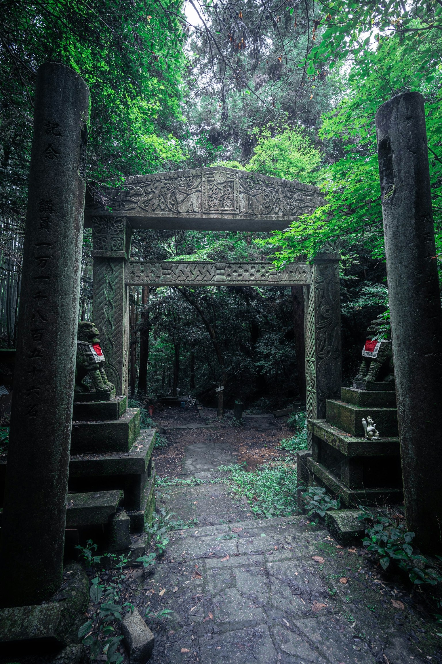 Sentiero misterioso con un torii in pietra e antiche sculture in pietra coperte di fogliame verde