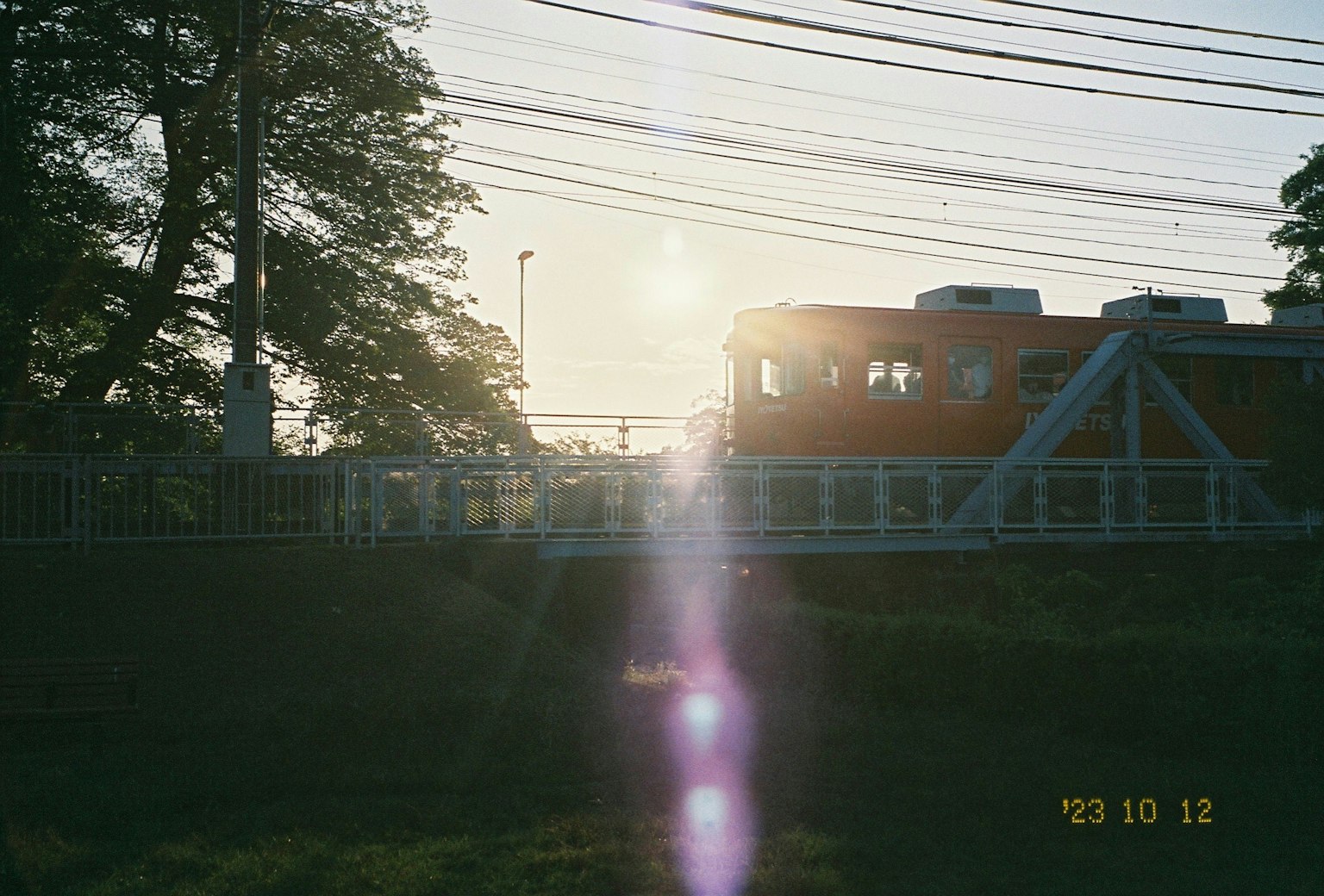 ทิวทัศน์พระอาทิตย์ตกของสะพานที่มีรถไฟสีส้มใกล้เคียง