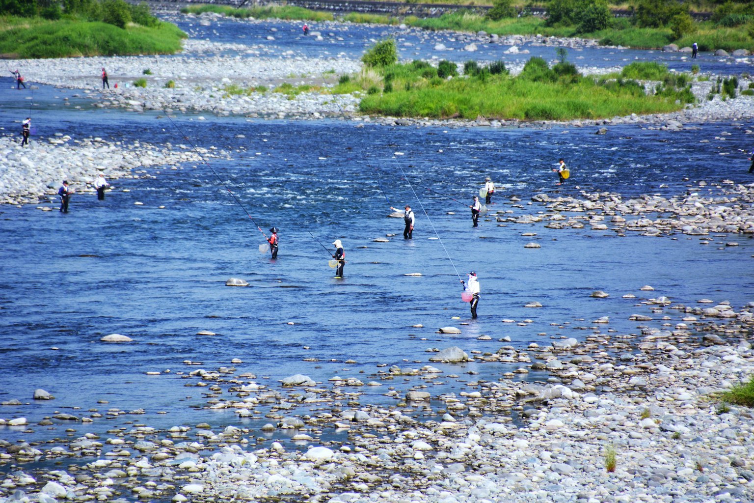 Personas pescando en un río rodeado de orillas rocosas y vegetación verde