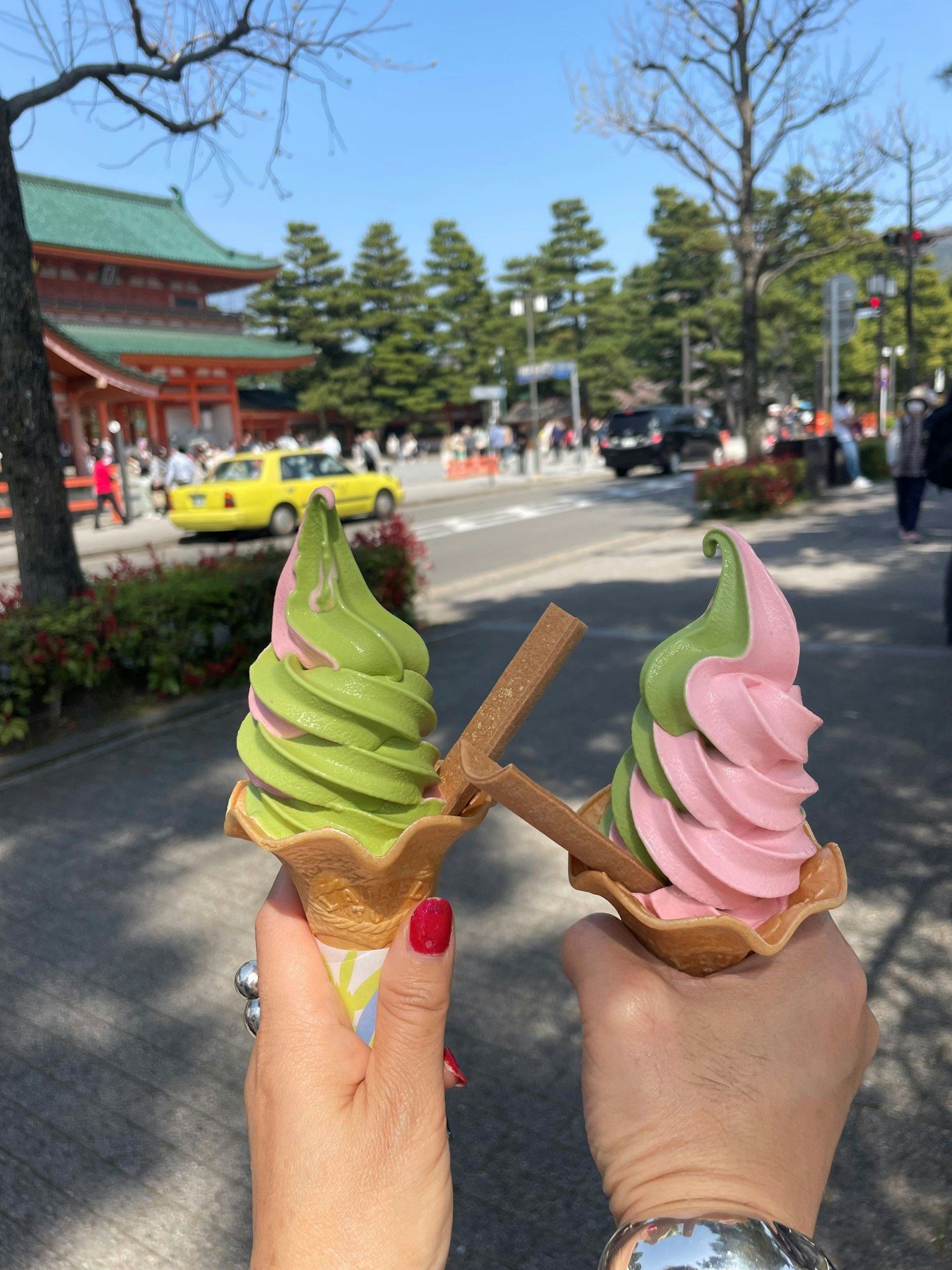 两只手握着绿色和粉色的软冰淇淋甜筒，背景是传统的日本建筑