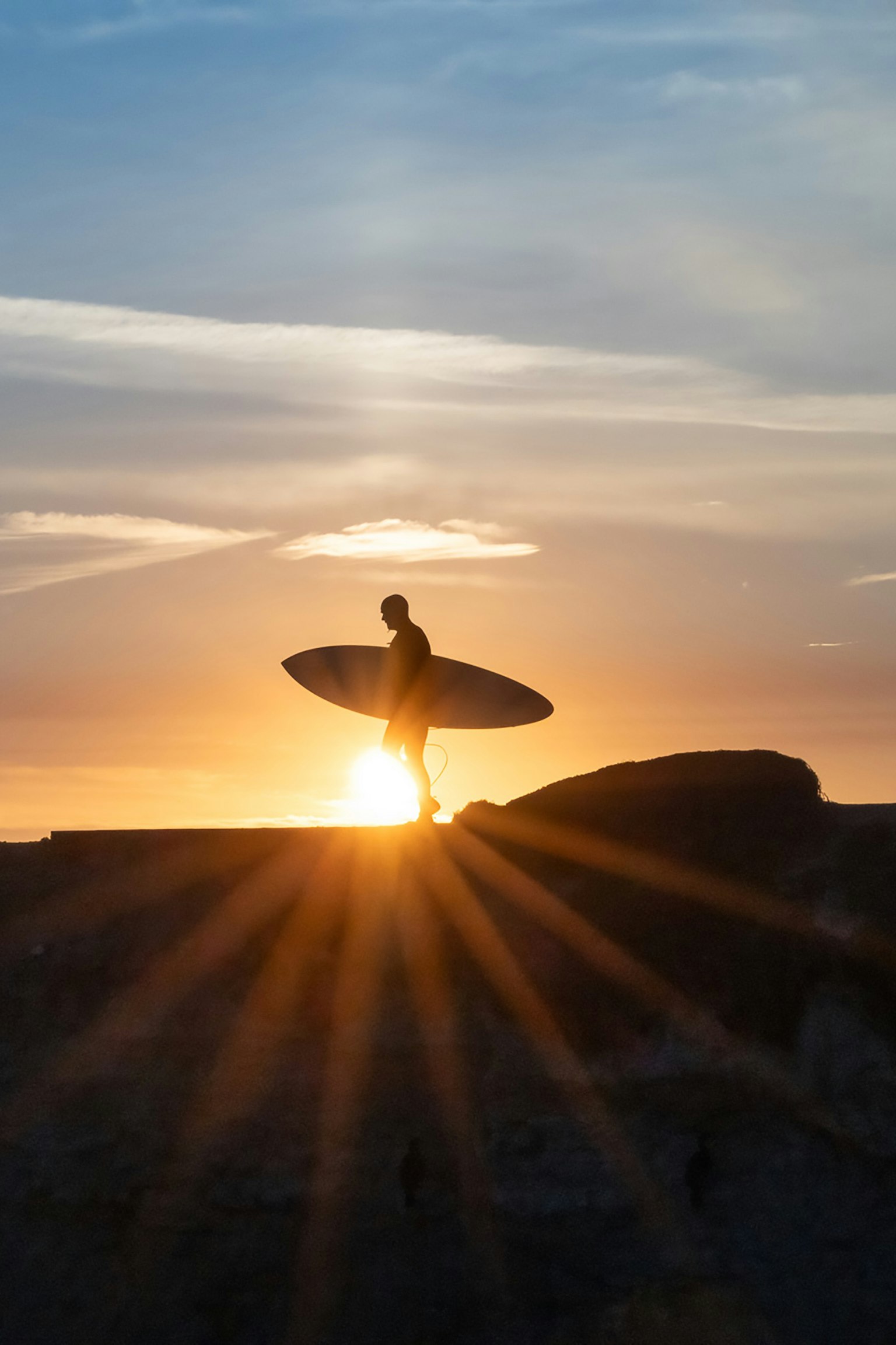 サーフボードを持ったサーフィンをする人が夕日を背にして立っているシルエット
