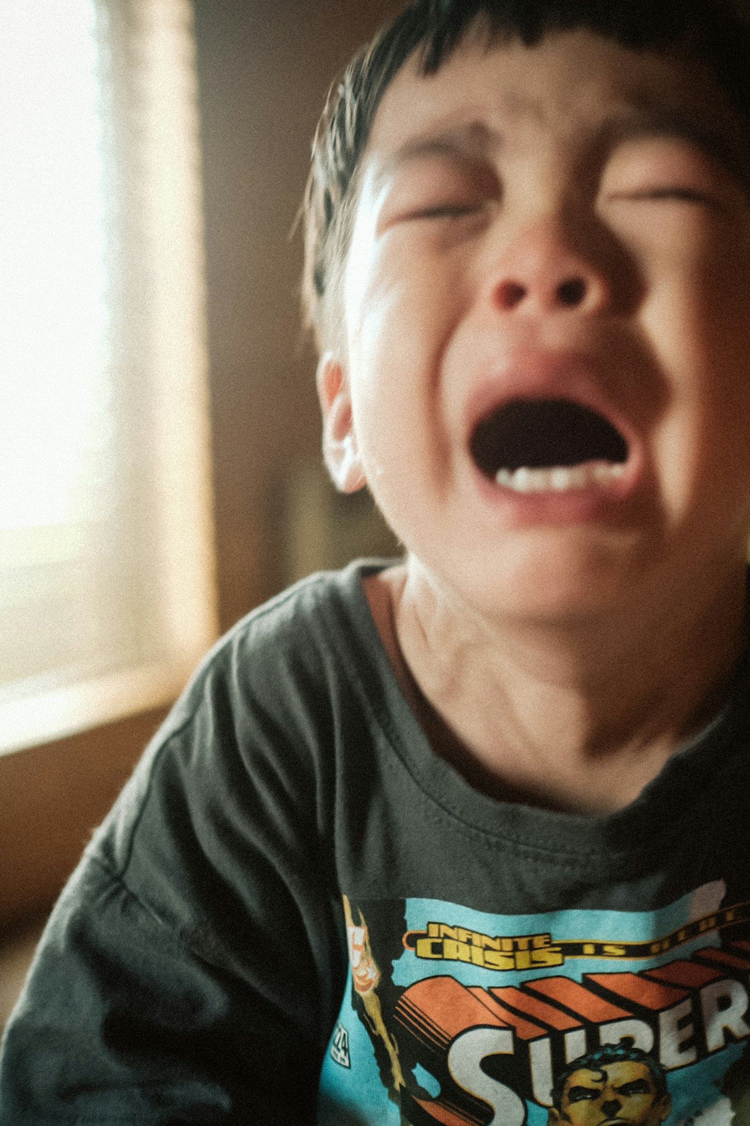 泣いている子供のクローズアップ 明るい窓の光が背景にある